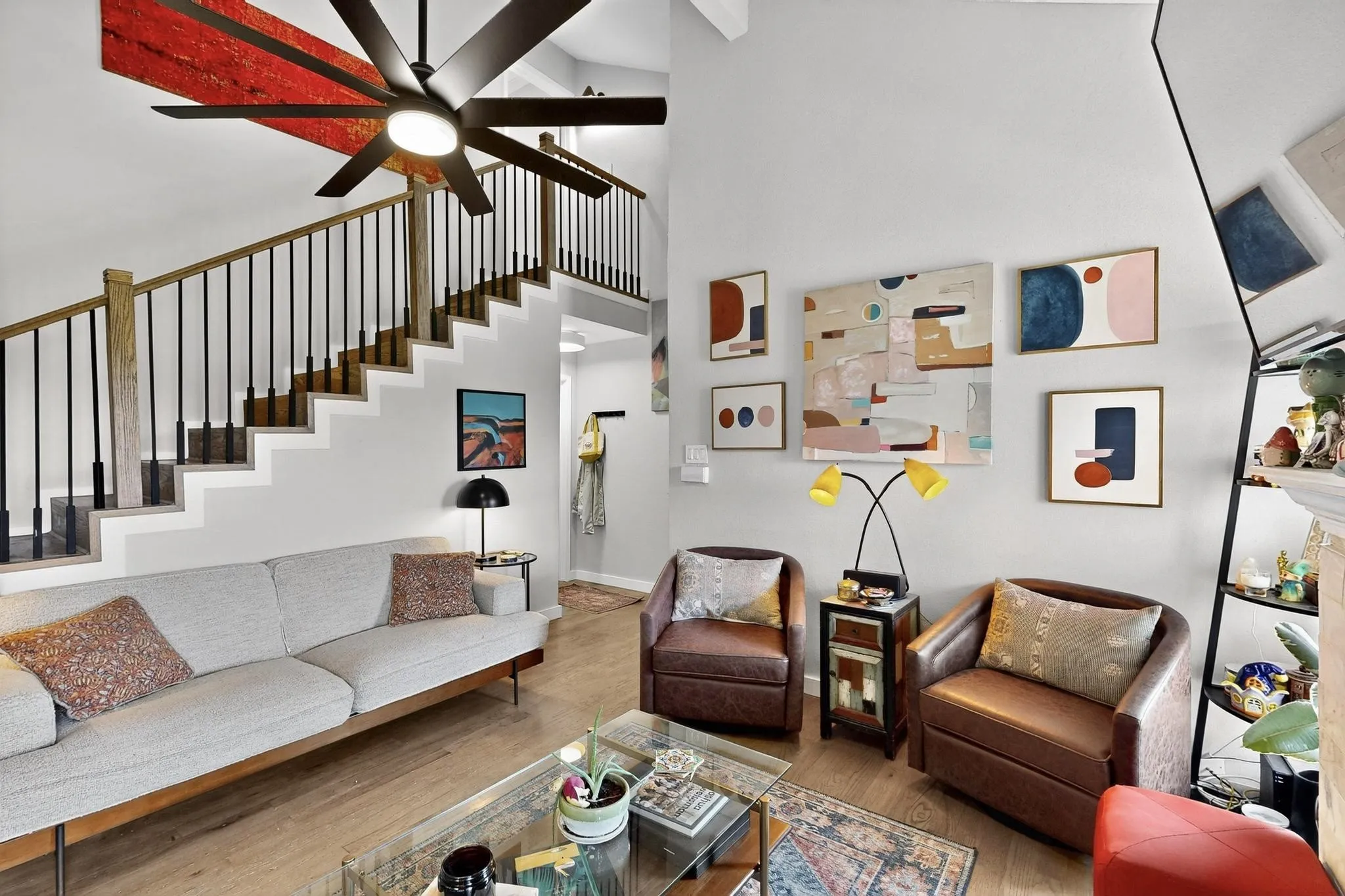 Living area featuring light wood-finish flooring, a two-story ceiling, and a prominent staircase with wood treads and black metal balusters
