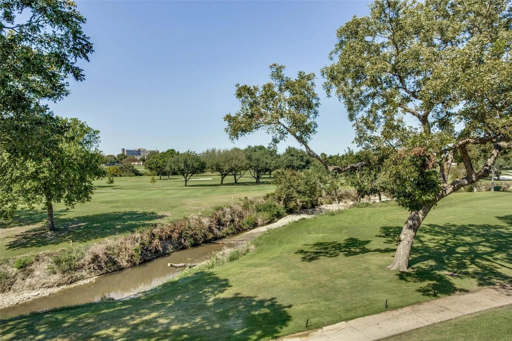 Expansive green space featuring a creek, mature trees, and a distant golf course