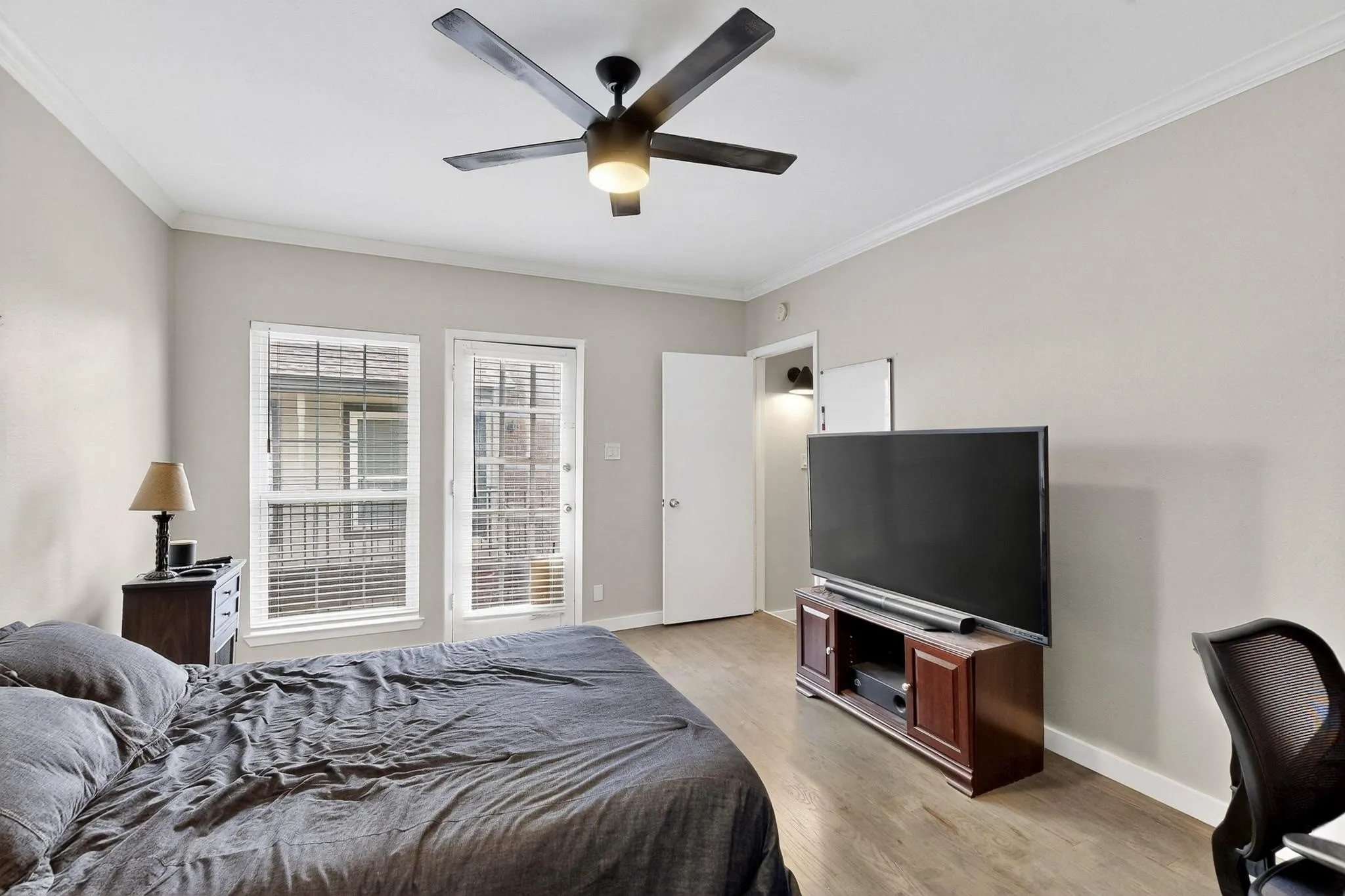 Spacious room featuring wood-finish flooring, a ceiling fan with integrated lighting, crown molding, and a paneled door with glass inserts