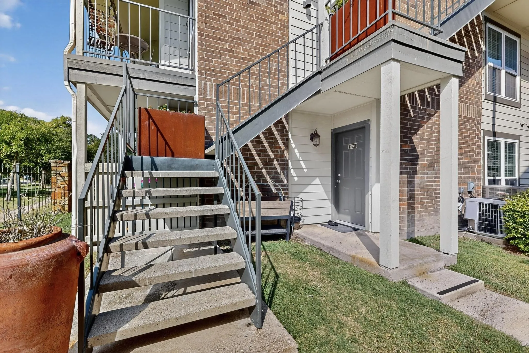 Exterior entry featuring a gray door with a decorative sconce, covered porch with white columns, and a concrete pathway