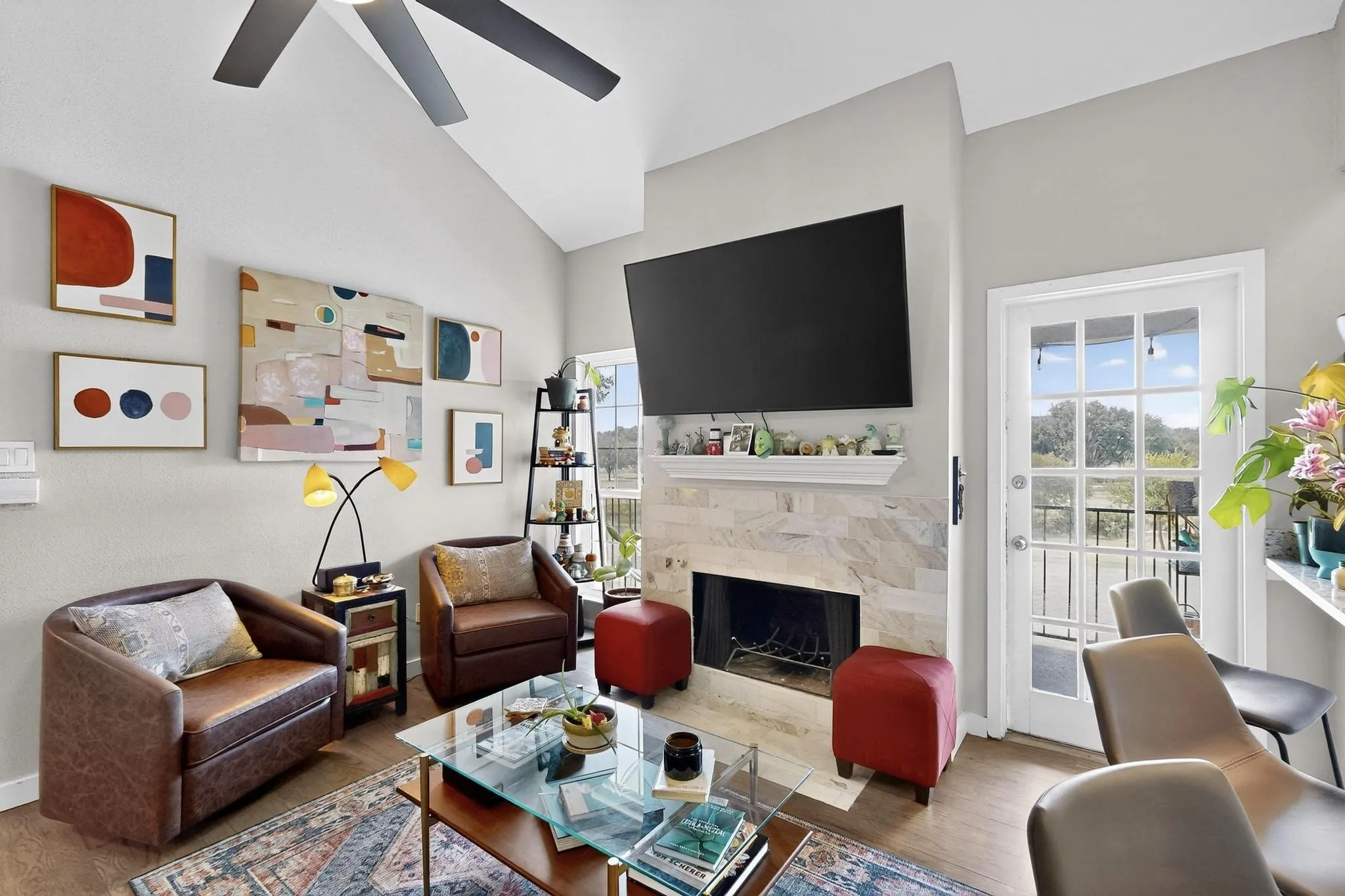 Living area featuring a vaulted ceiling with a ceiling fan, a fireplace with a stone surround and mantel, and wood-finish flooring