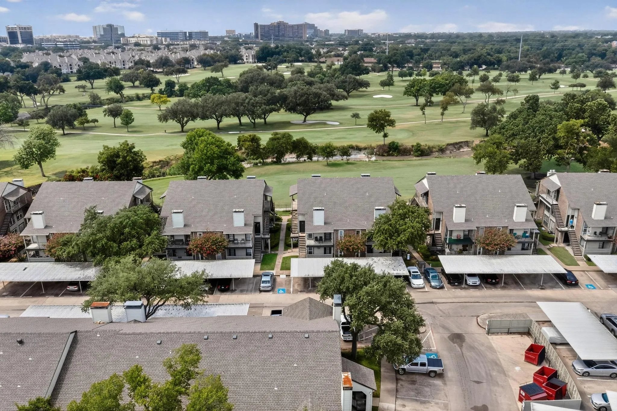 Multi-story buildings with pitched roofs and multiple balconies, featuring covered parking areas and a prominent golf course backdrop