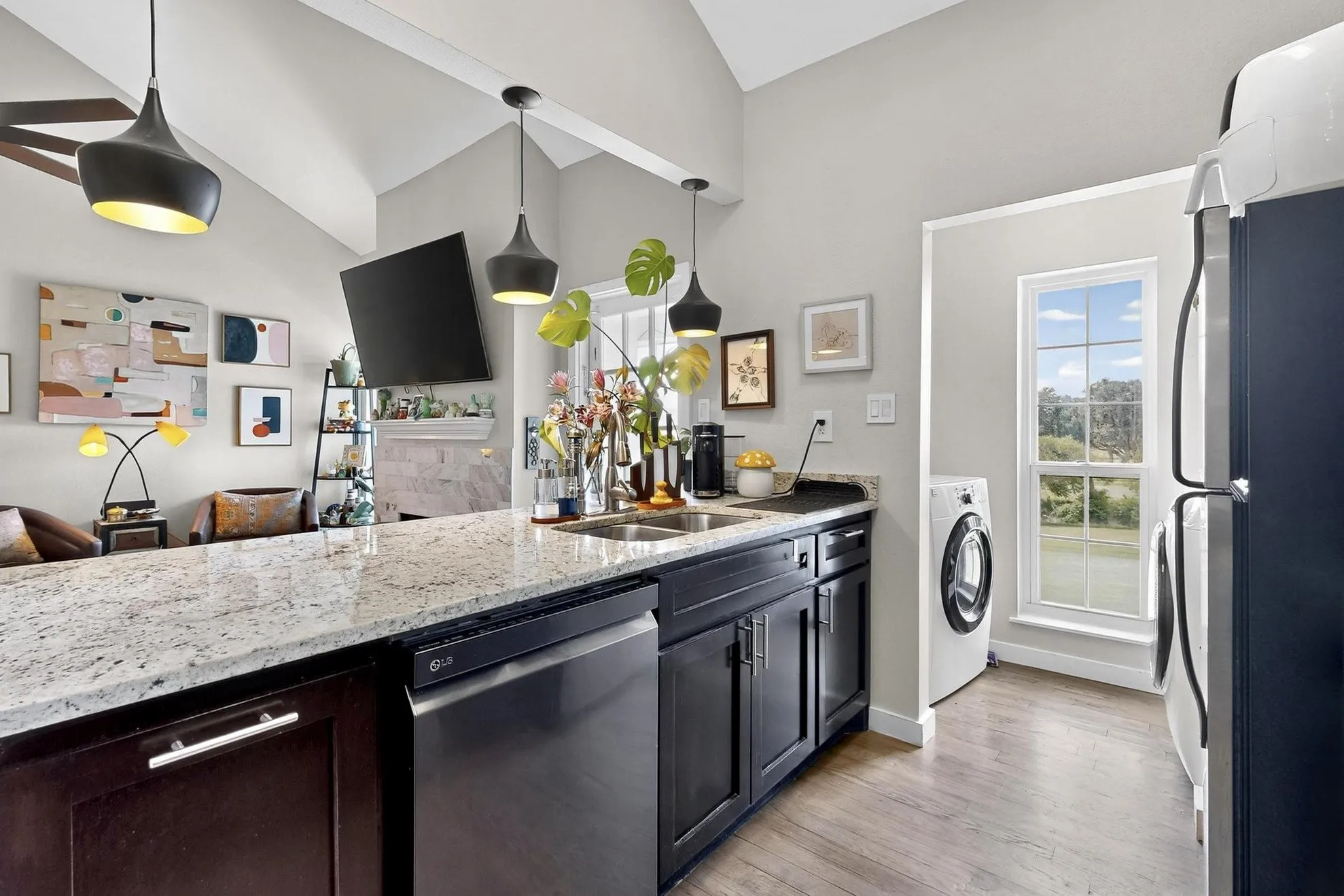 Kitchen featuring a spacious island with a light-toned countertop, dark wood-finish cabinetry, stainless steel dishwasher, and an integrated sink