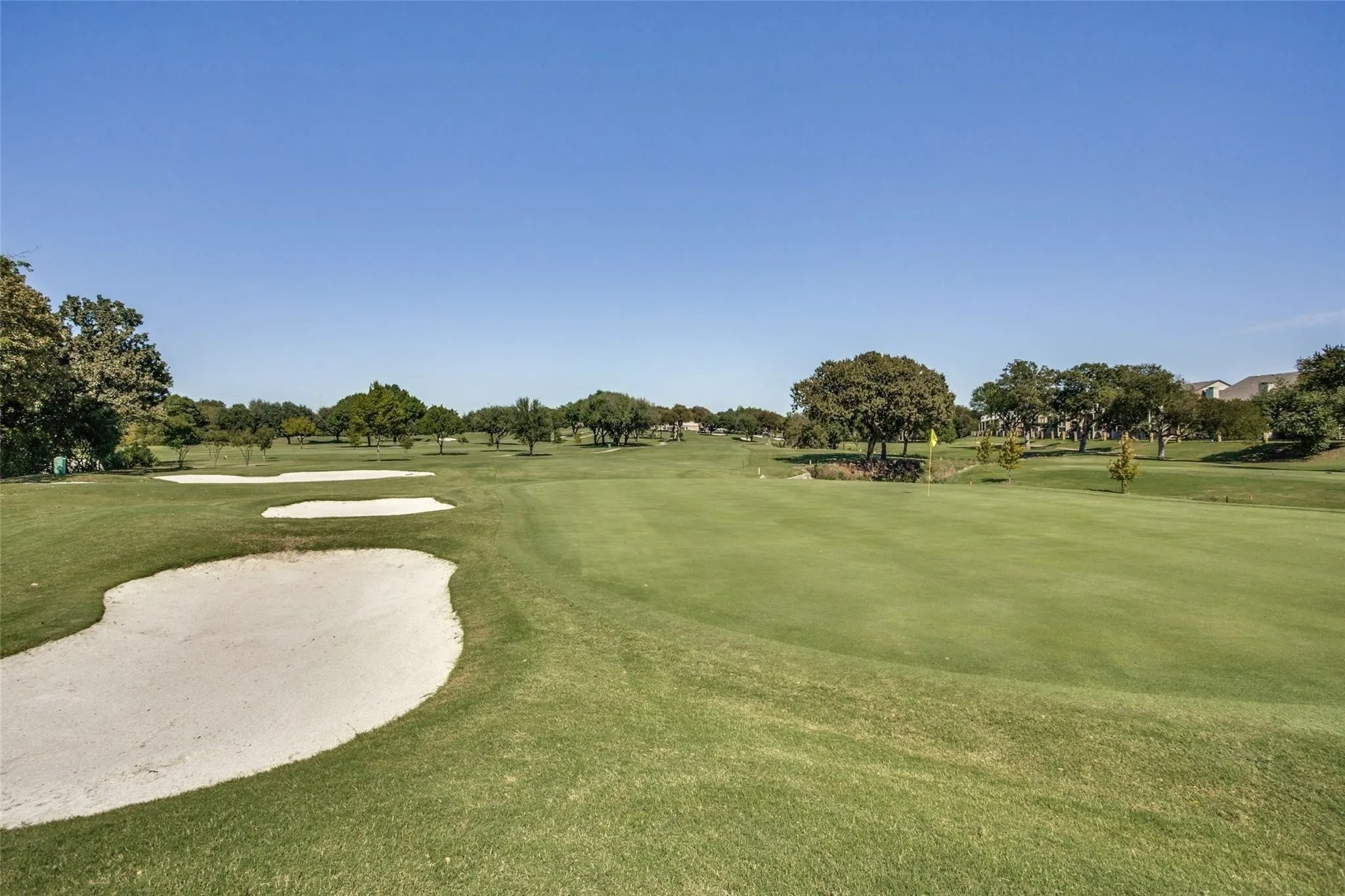 Expansive golf course setting featuring manicured greens, sand bunkers, and mature trees