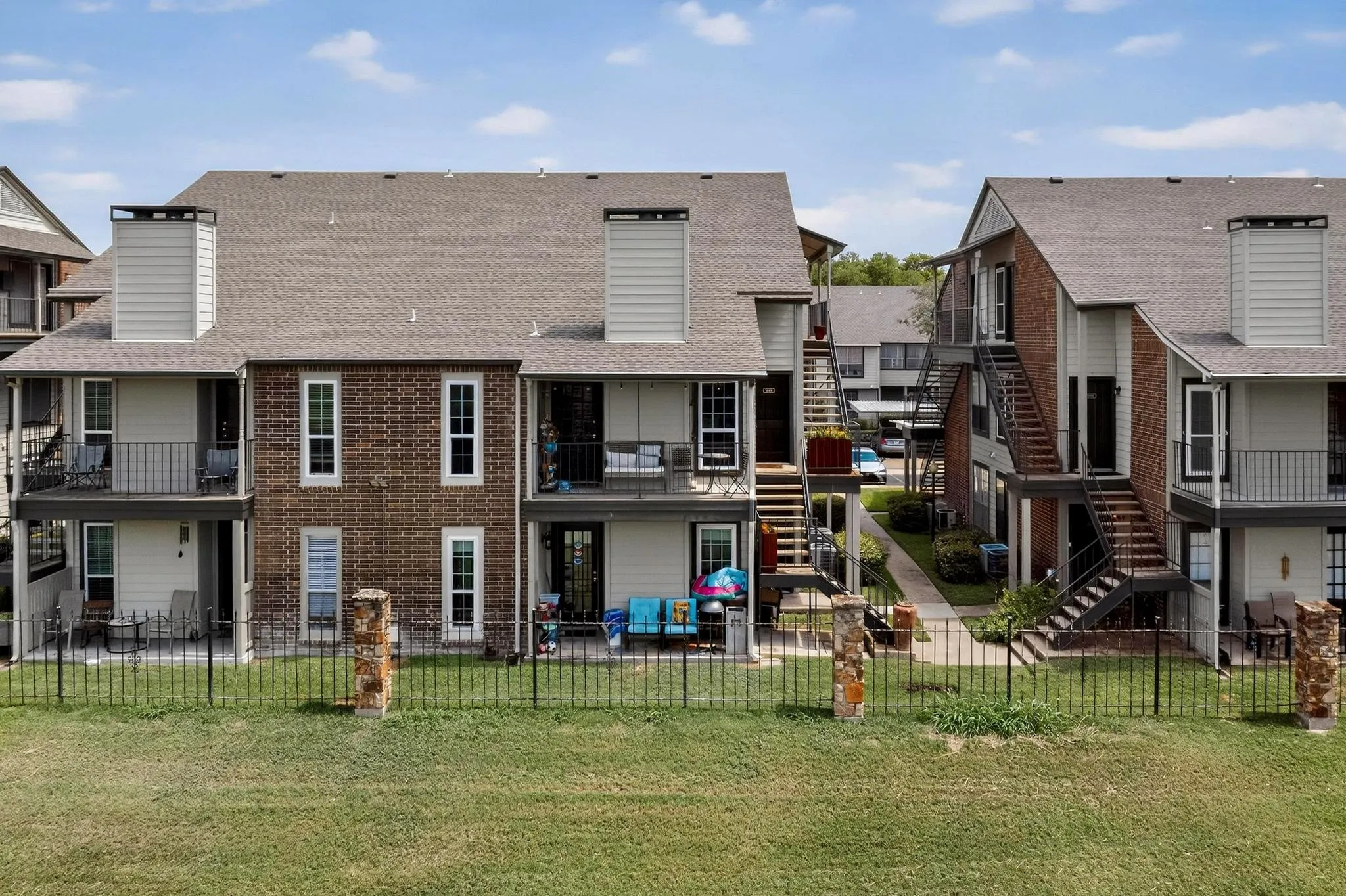 Multi-story apartment building featuring brick and siding exteriors, private balconies and patios, and a shared green space