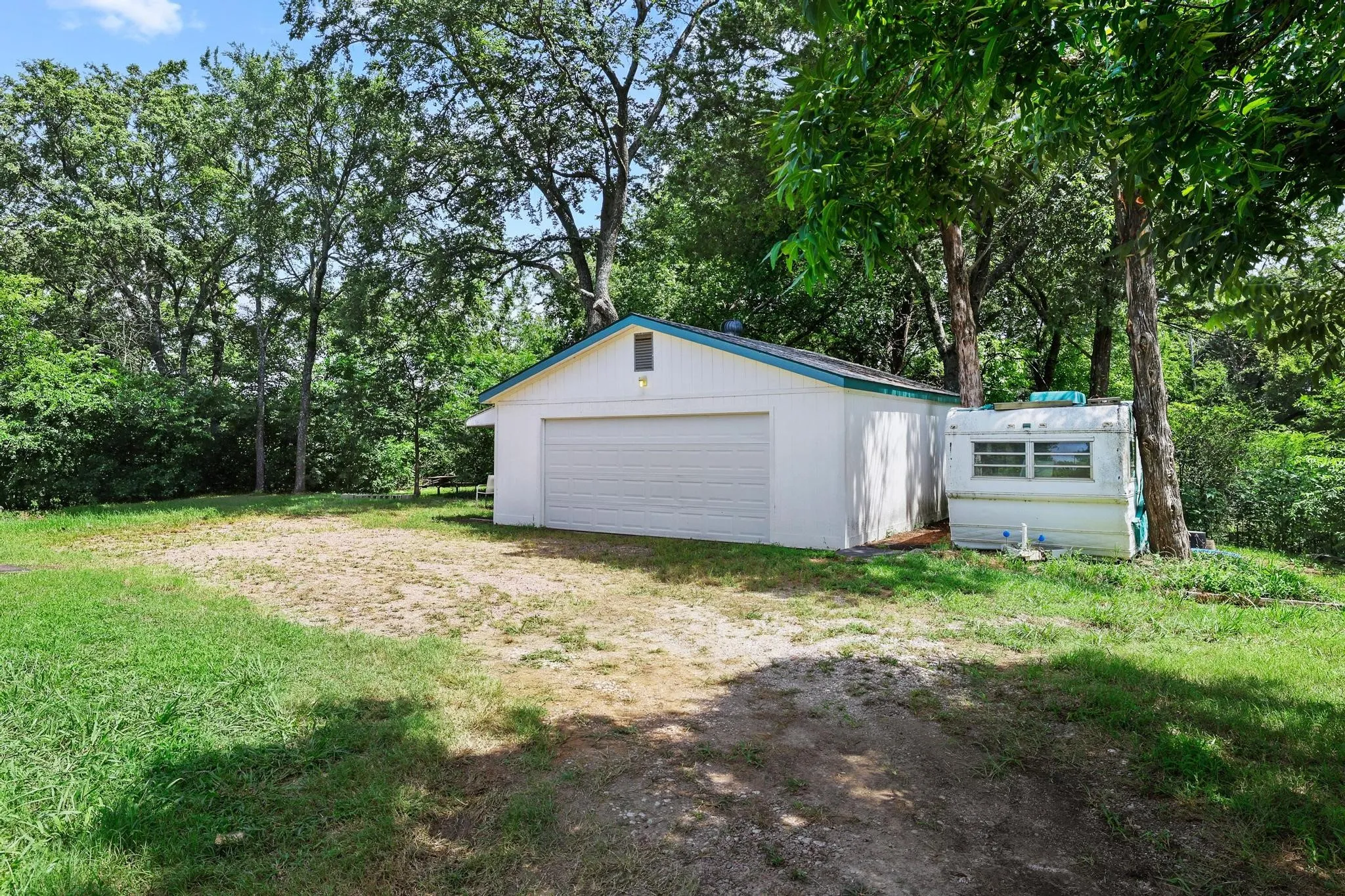 Detached garage with a single roll-up door, white siding, and a teal-trimmed gable roof