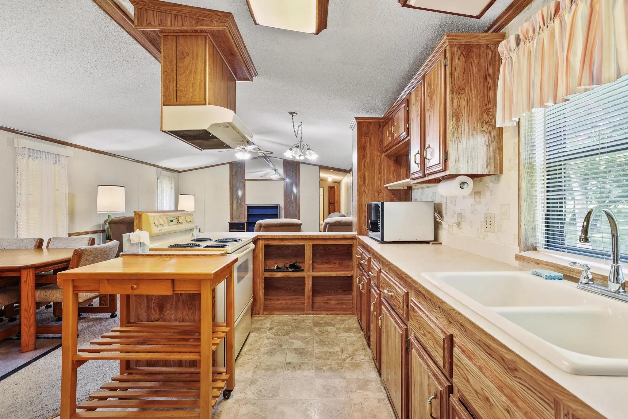 Kitchen featuring wood-finish cabinetry, a double basin sink, and an electric range with an overhead vent hood
