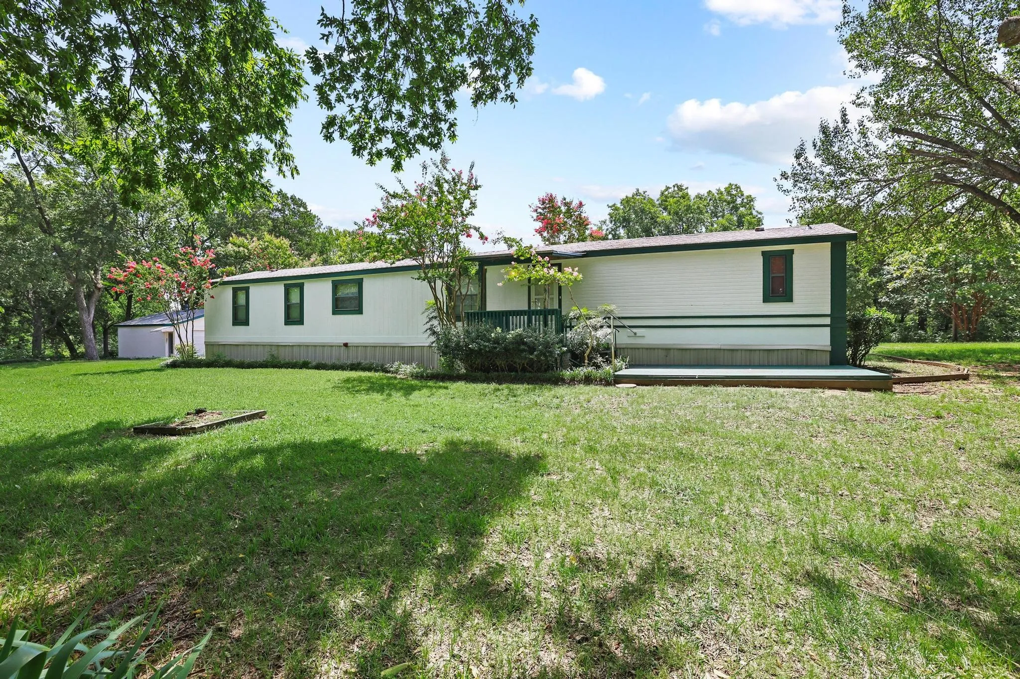 White siding home with green trim, featuring a front porch with railing, an additional side deck, and a detached storage shed