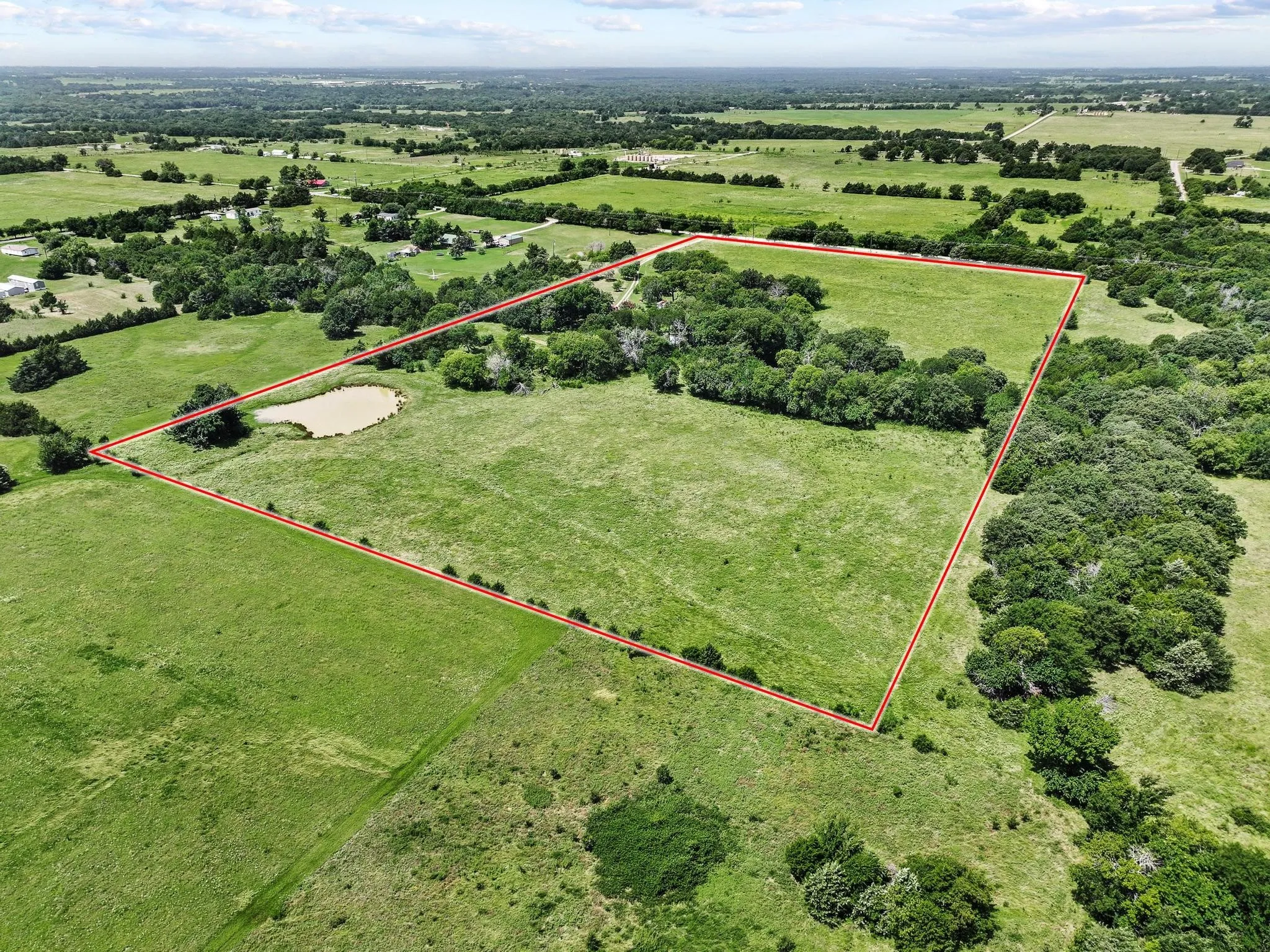 Back view of acreage featuring a private pond, open pastures, and mature tree lines