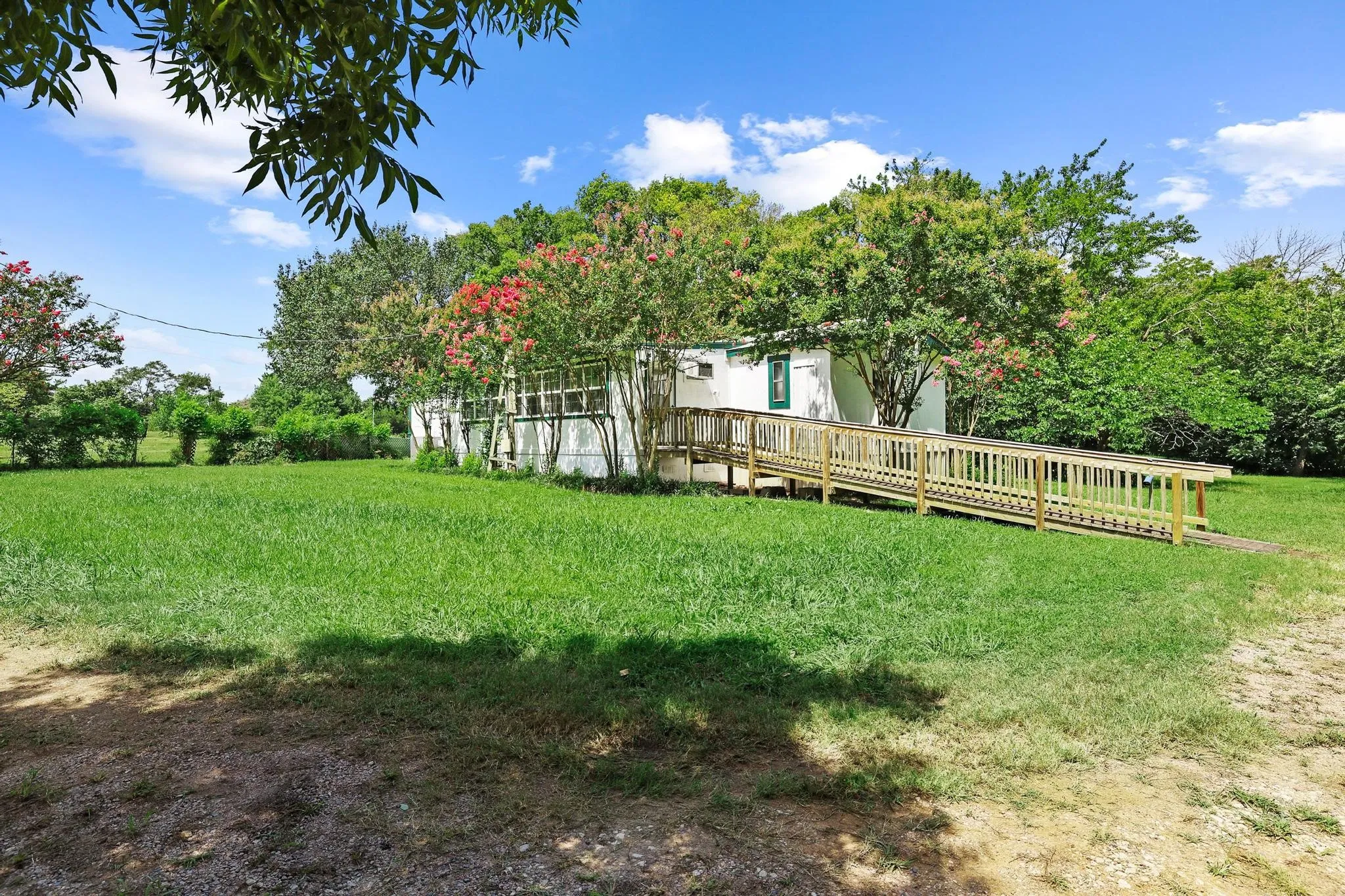Well-maintained lawn space featuring mature trees and a wooden access ramp leading to the building entrance