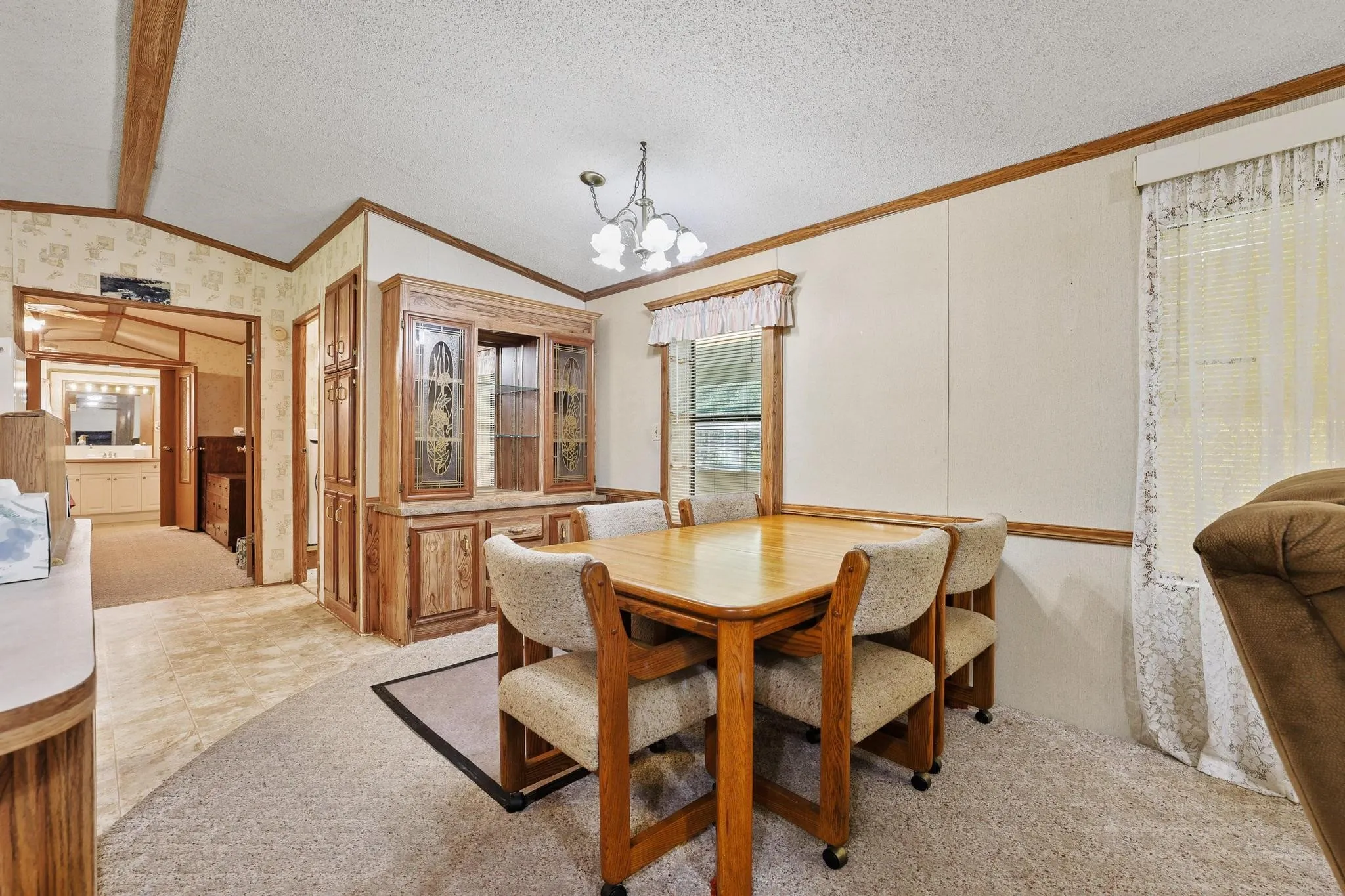 Dining area featuring a built-in wood-finish hutch with glass-front cabinetry, a window with horizontal blinds, and a multi-light ceiling fixture