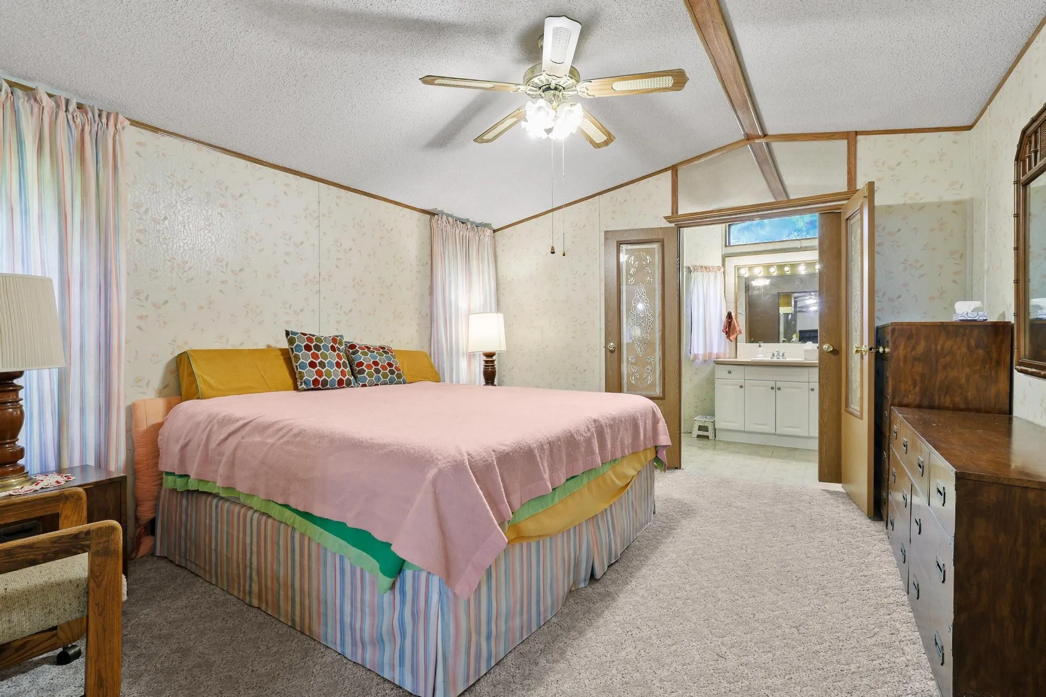 Carpeted bedroom featuring a ceiling fan with light, decorative wallpaper, and wood-finish trim