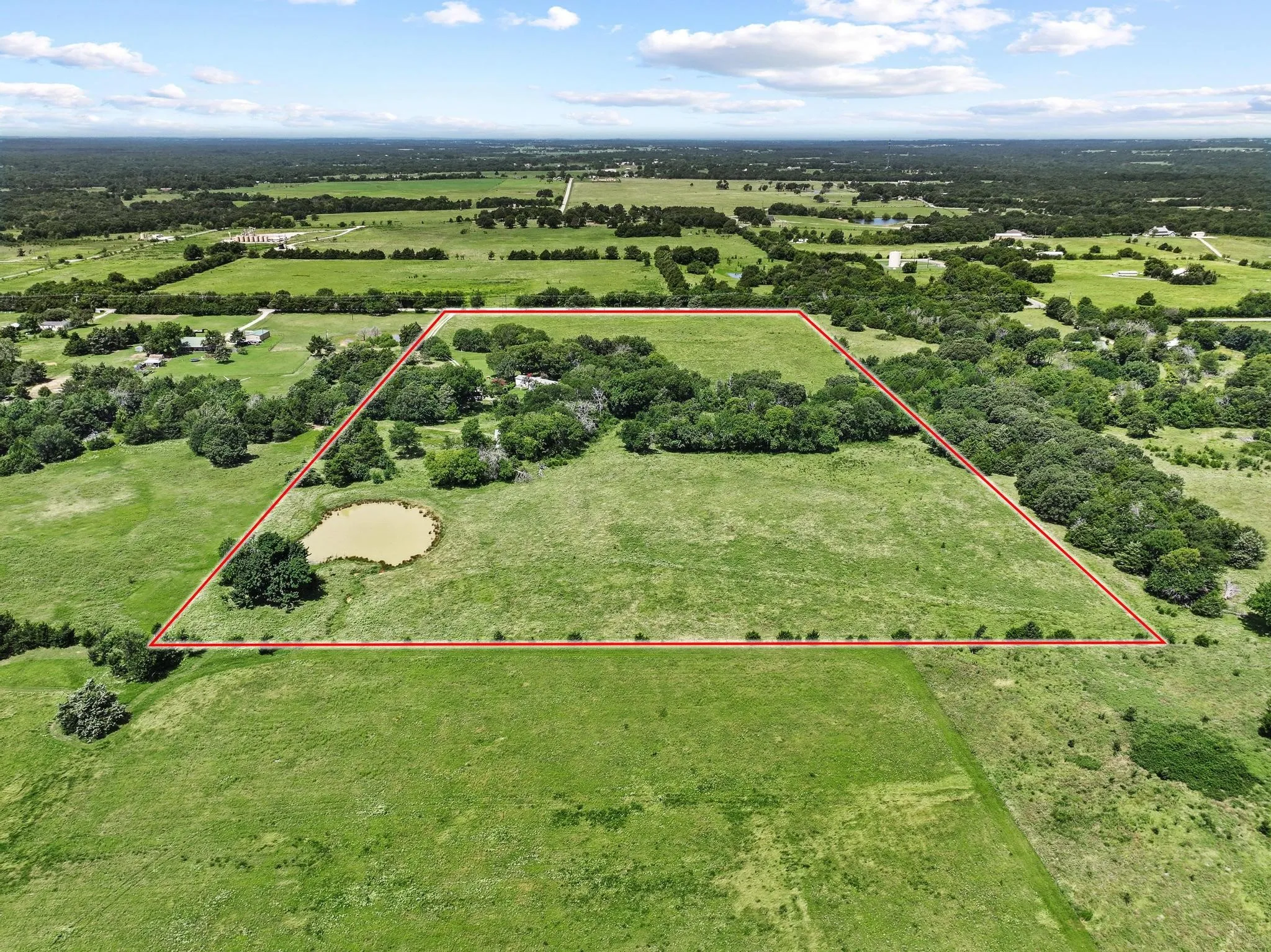 Acreage featuring mature trees, open grassy areas, and a visible pond