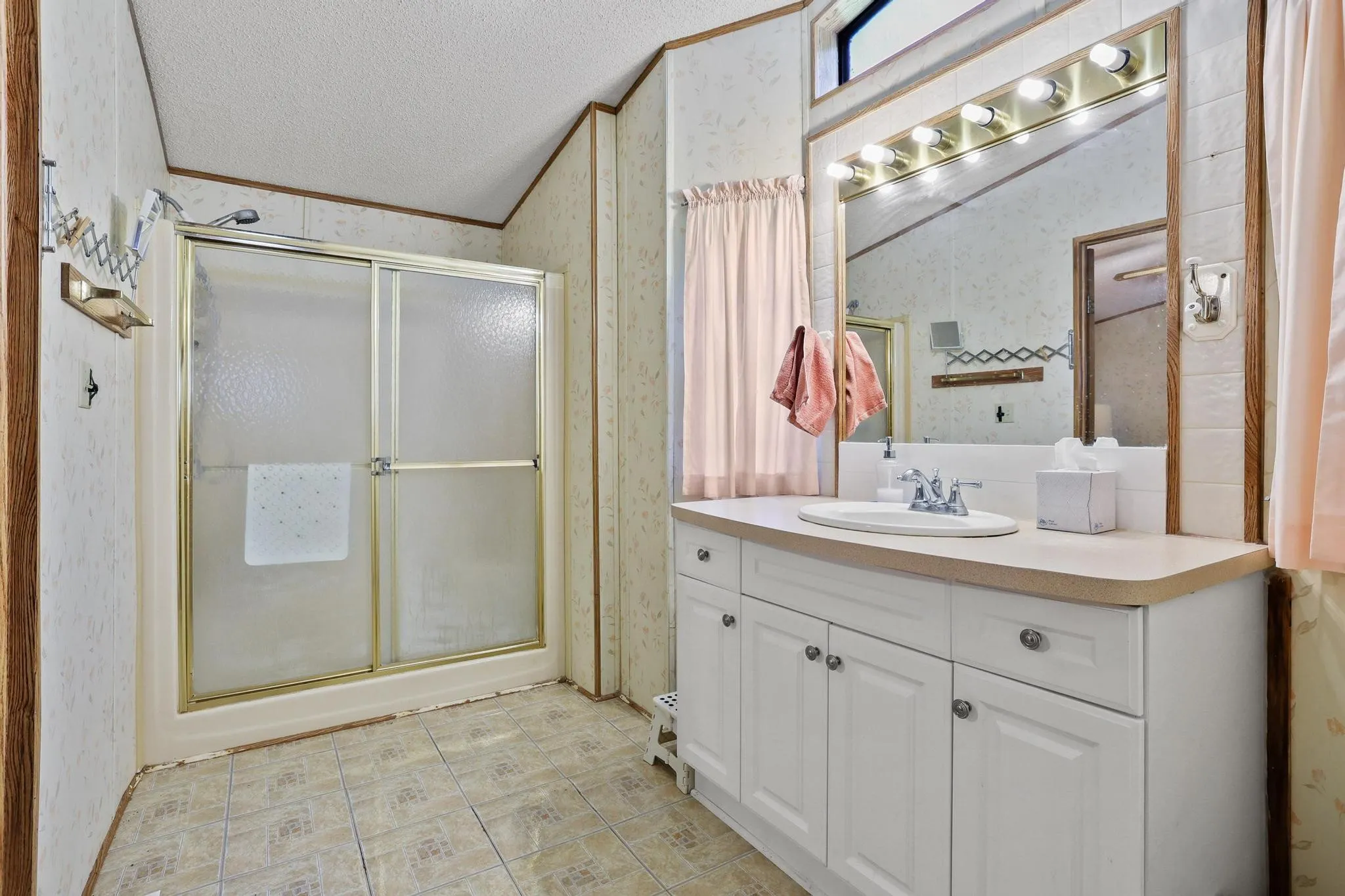 Bathroom featuring a single vanity with white cabinetry, a large mirror, and a shower with sliding glass doors