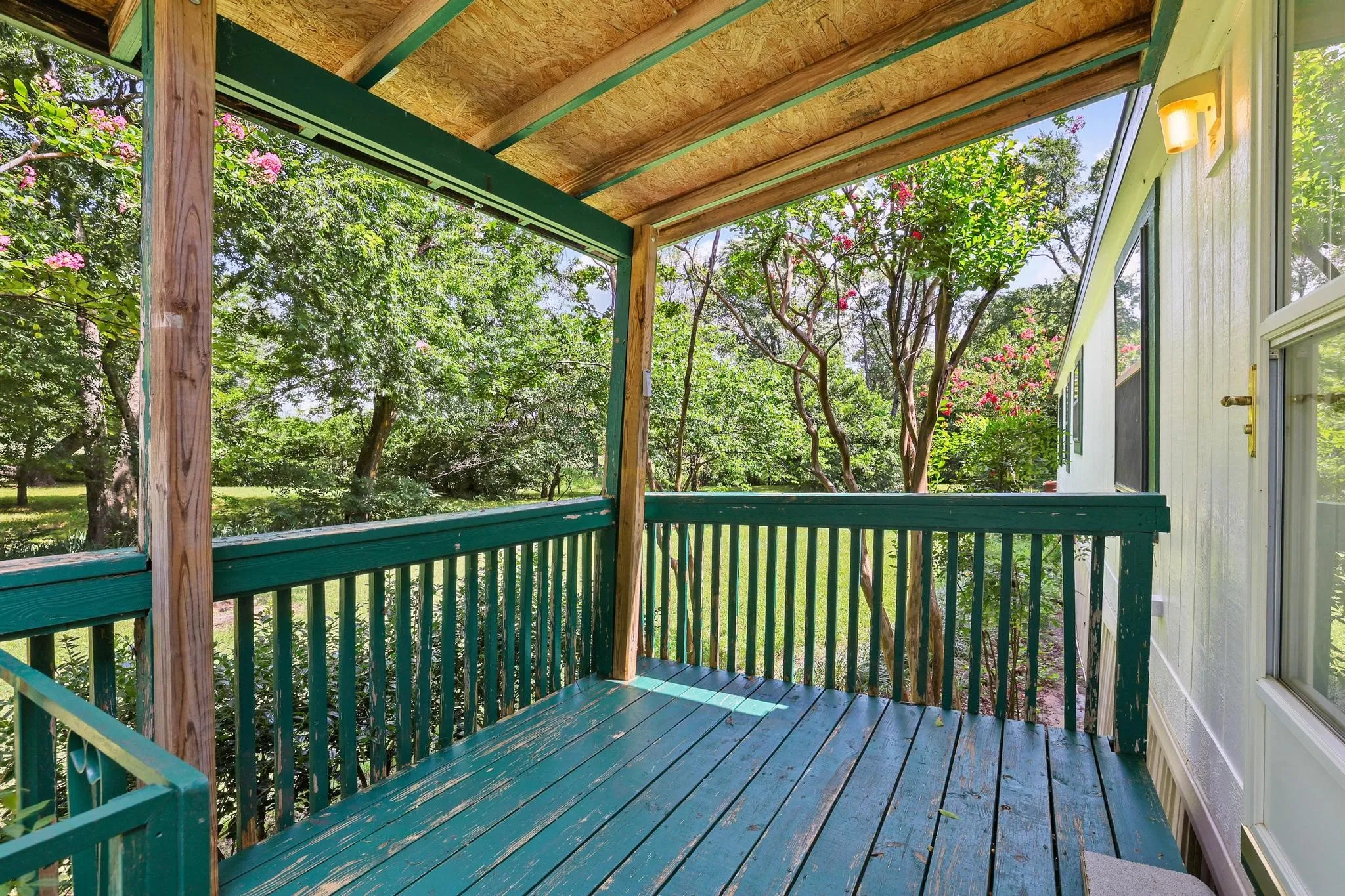 Covered outdoor deck with painted wood flooring and railings, featuring natural wood support beams and a wood-finish ceiling