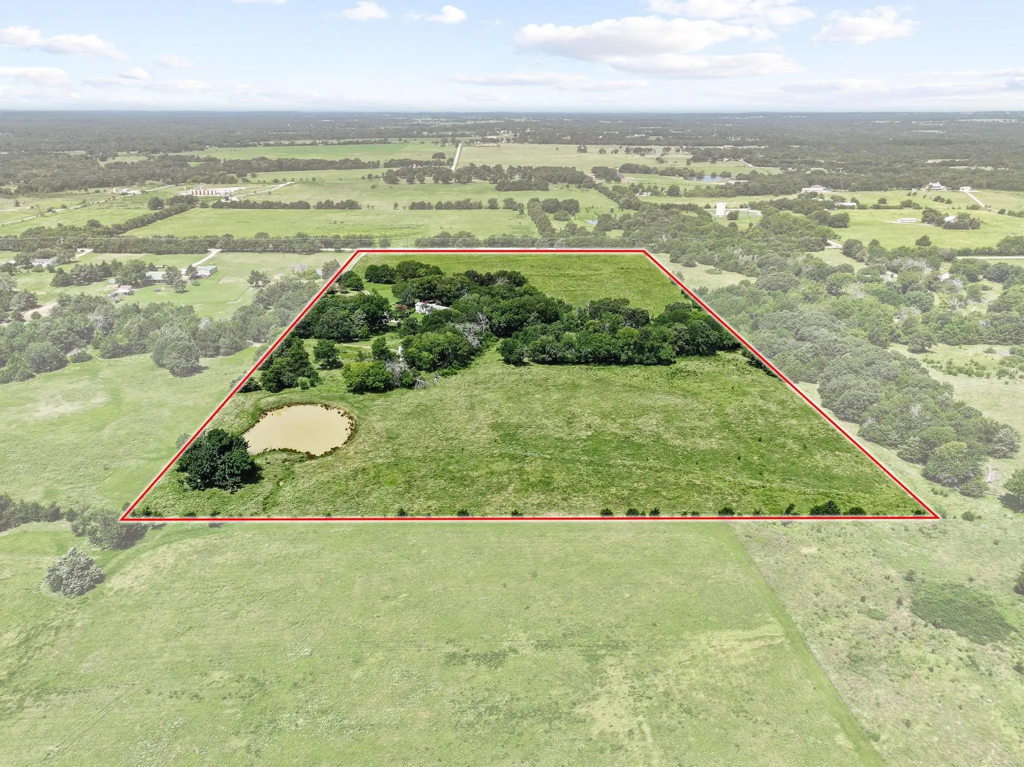 Acreage featuring a natural pond, mature tree clusters, and open grassy fields