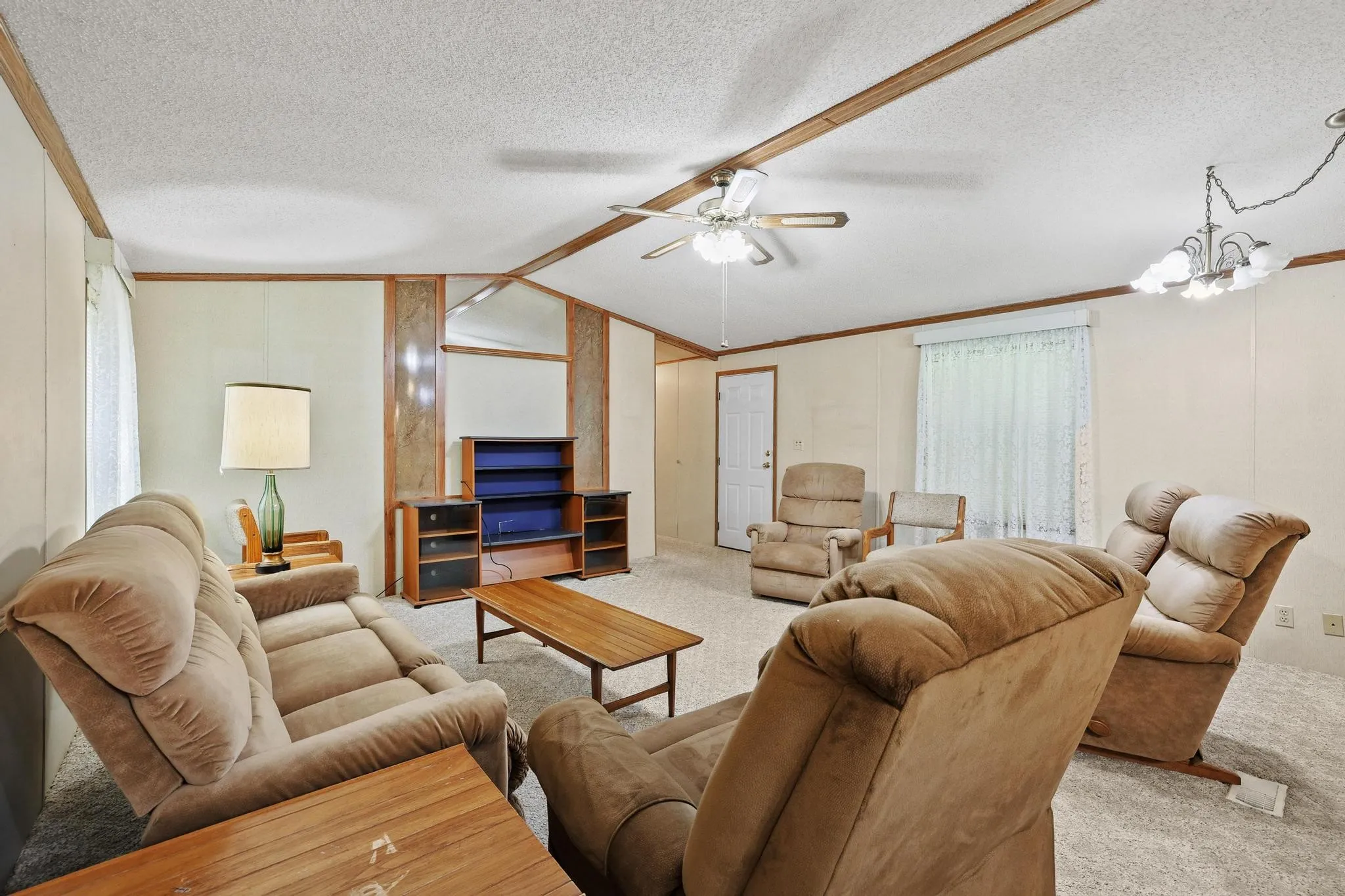 Carpeted living area featuring a ceiling fan, wood-finish ceiling beams, and a decorative light fixture
