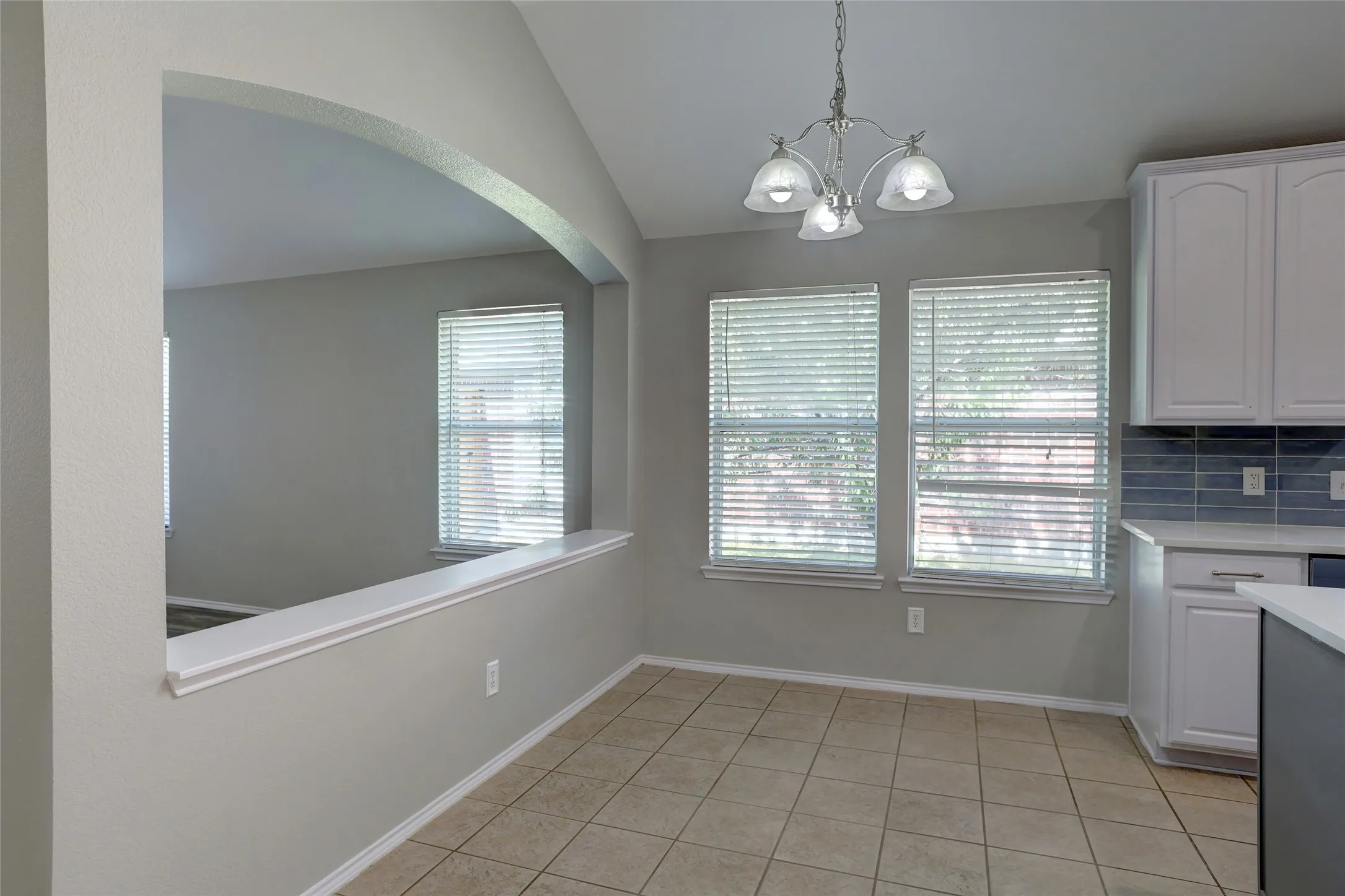 Open-concept dining area featuring tile flooring, a contemporary chandelier, and a pass-through arched opening to an adjacent space