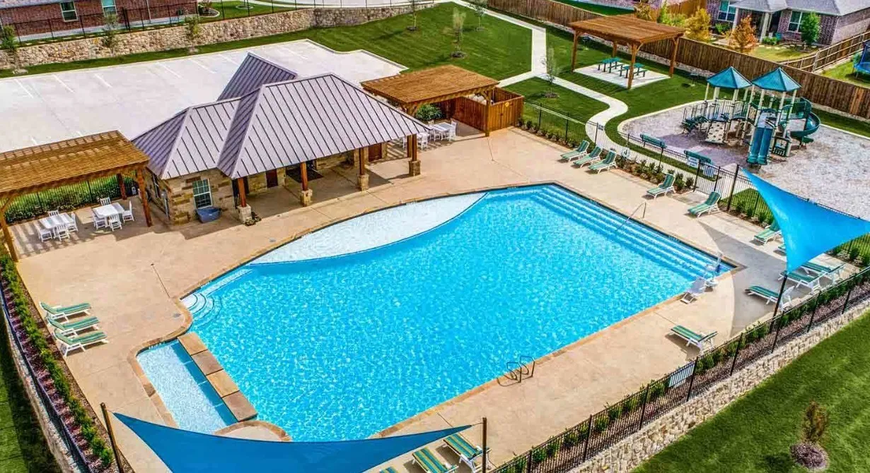 Resort-style pool area featuring a large swimming pool with concrete decking, an adjacent shaded pergola, and a stone-clad amenity building