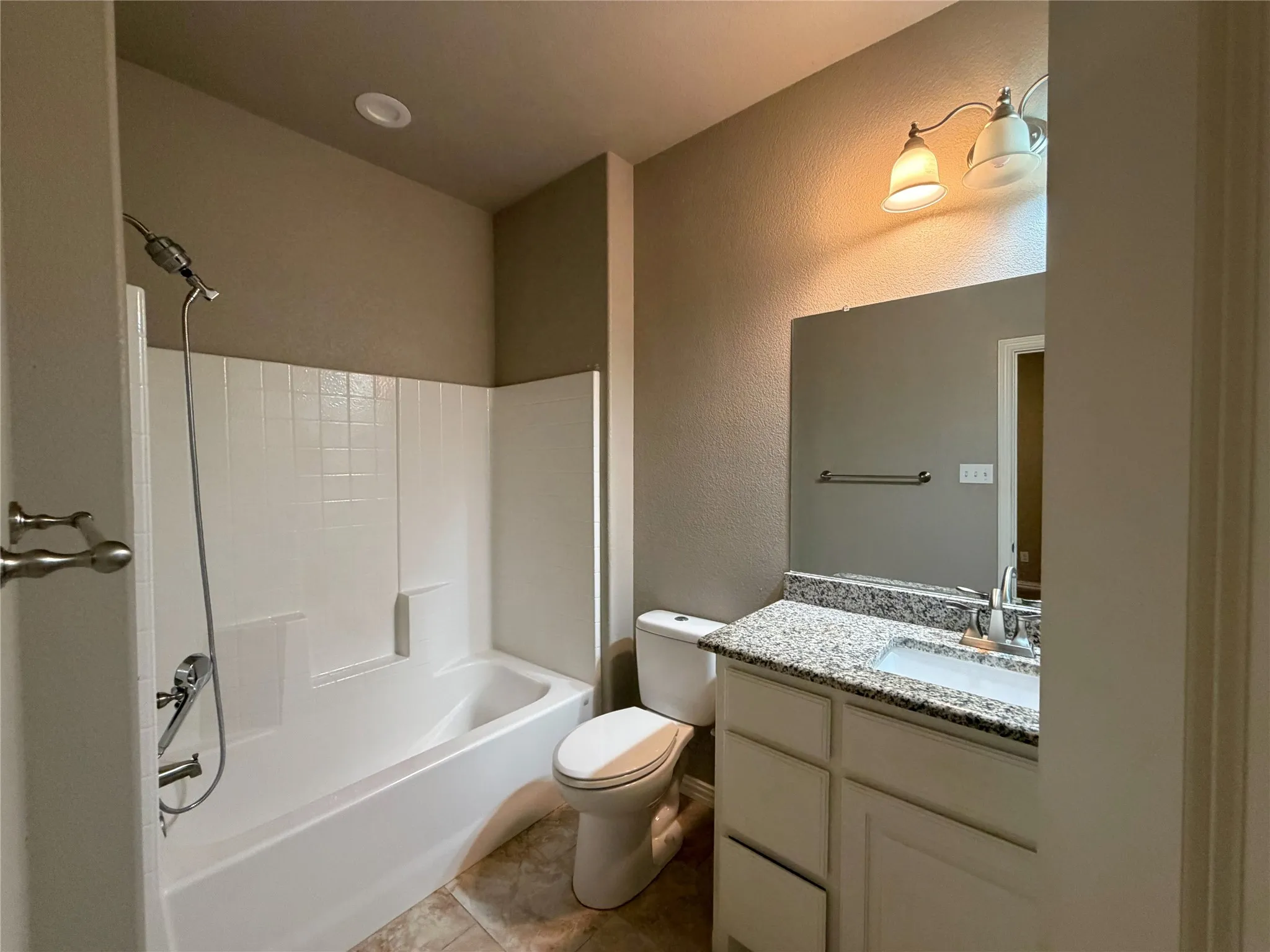 Bathroom featuring a white tub/shower combination, a vanity with a granite-style countertop, an undermount sink, and a framed mirror