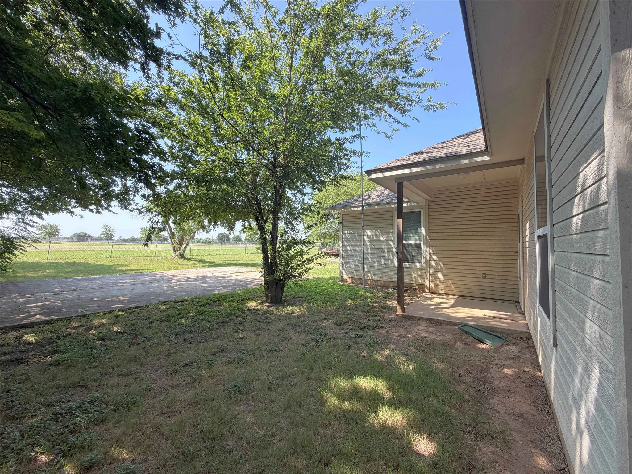 Exterior patio area featuring a concrete surface, tan siding, and a partial roof overhang