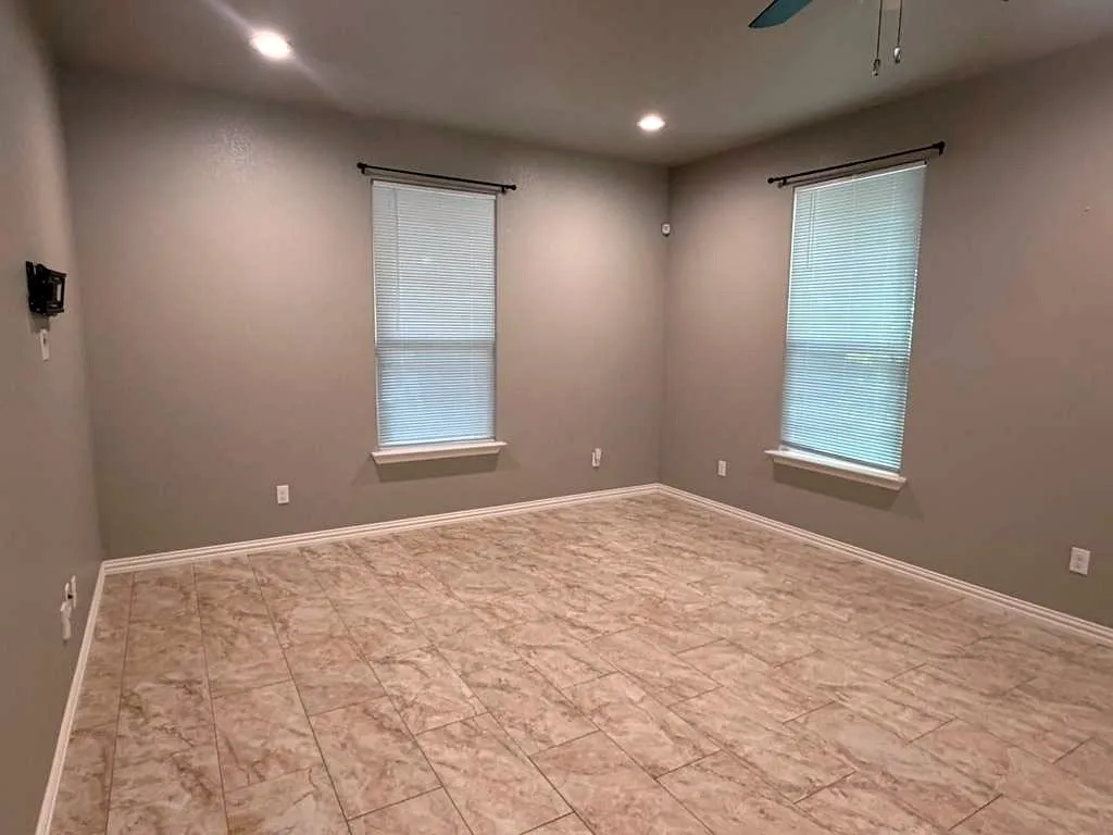Spacious room featuring tile flooring, neutral wall tones, and two windows with blinds