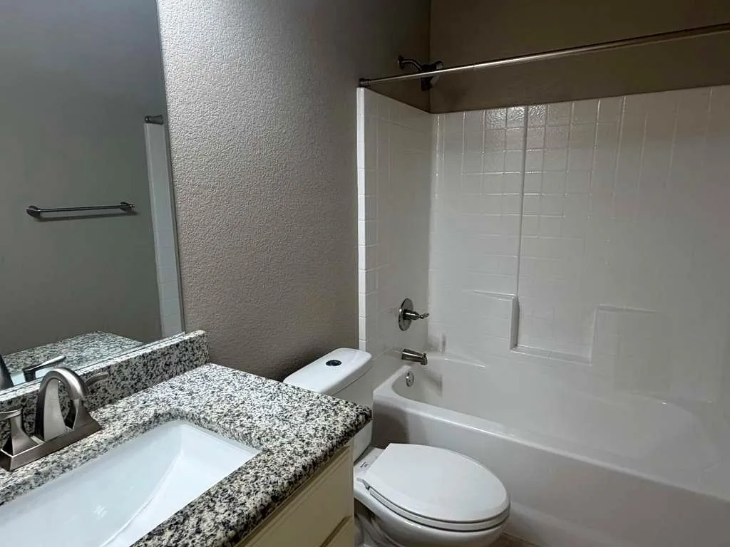 Bathroom featuring a full-size bathtub with integrated shower, white tile surround, and a brushed nickel showerhead