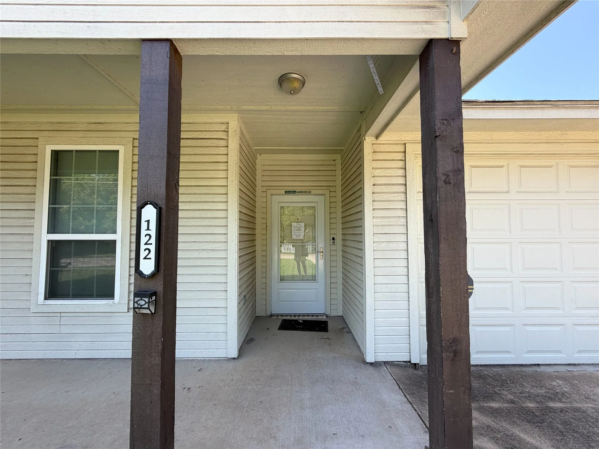 Covered entry with two substantial wood-finish columns, white siding, and an overhead light fixture
