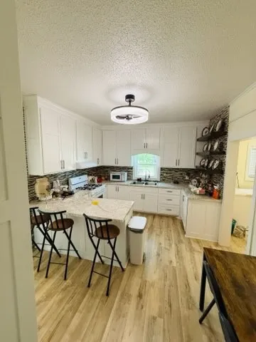Kitchen featuring extensive white cabinetry, light-toned wood-finish flooring, a U-shaped countertop, a tile backsplash, and a modern ceiling light fixture