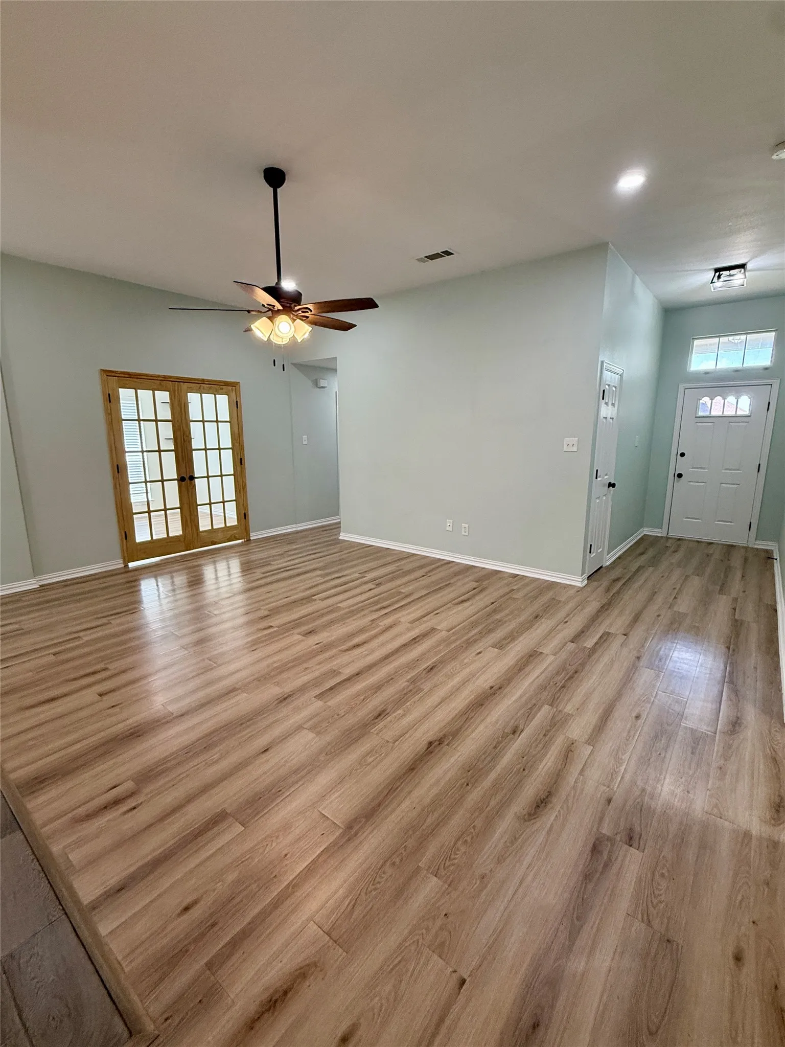 Spacious room featuring wood-finish flooring, light-toned walls, a ceiling fan with integrated lighting, recessed lighting, and white baseboards