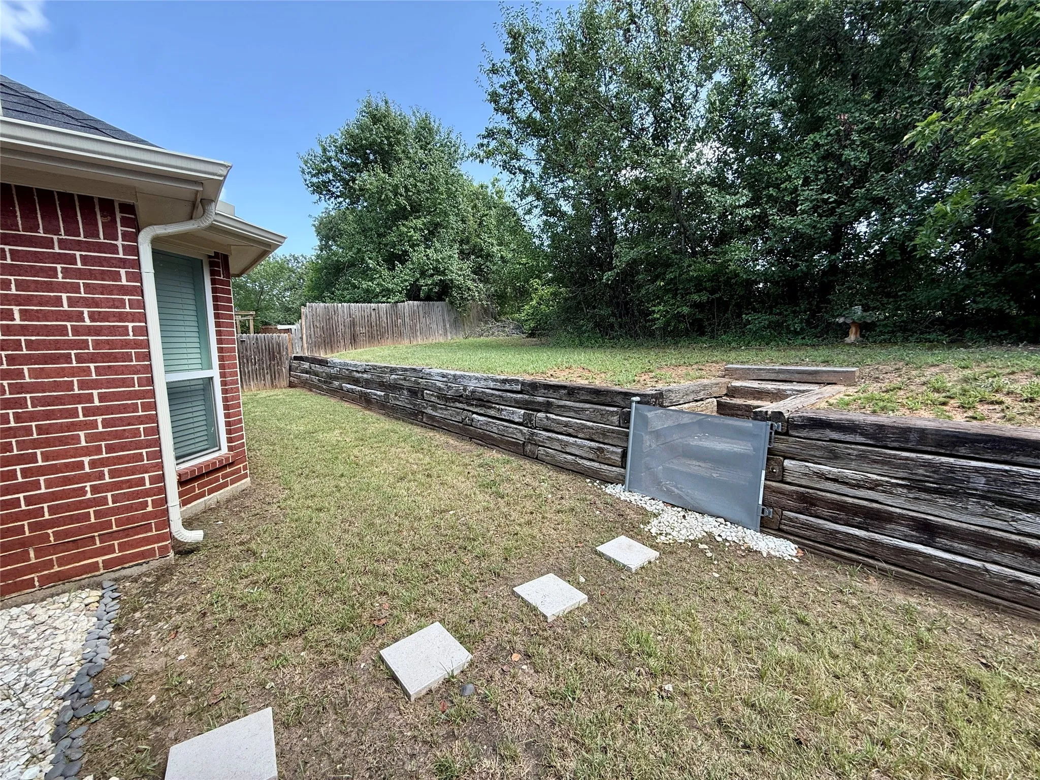 Tiered backyard featuring wood retaining walls and a gravel-filled drainage area