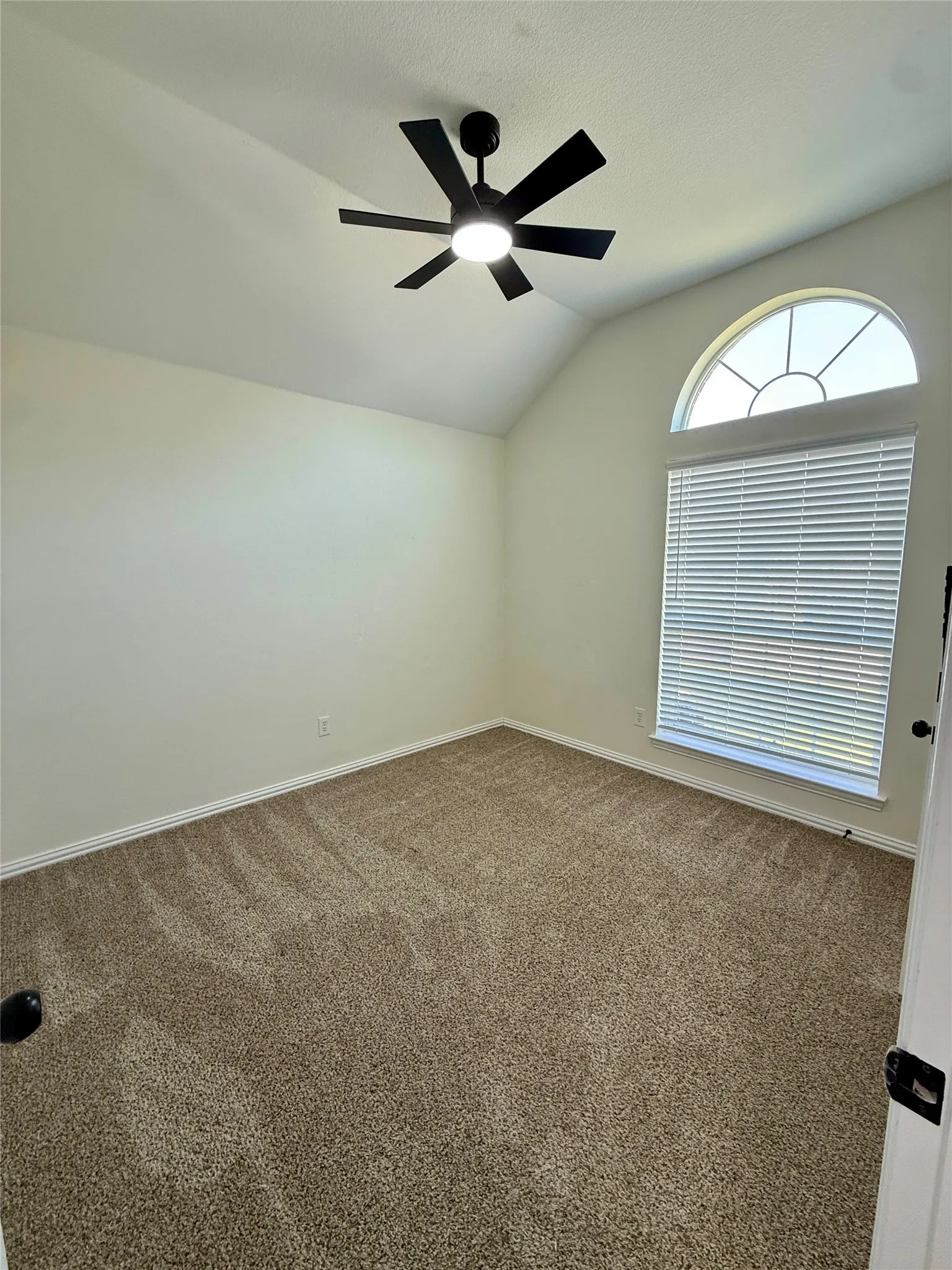 Room featuring a vaulted ceiling and a modern black ceiling fan with integrated lighting