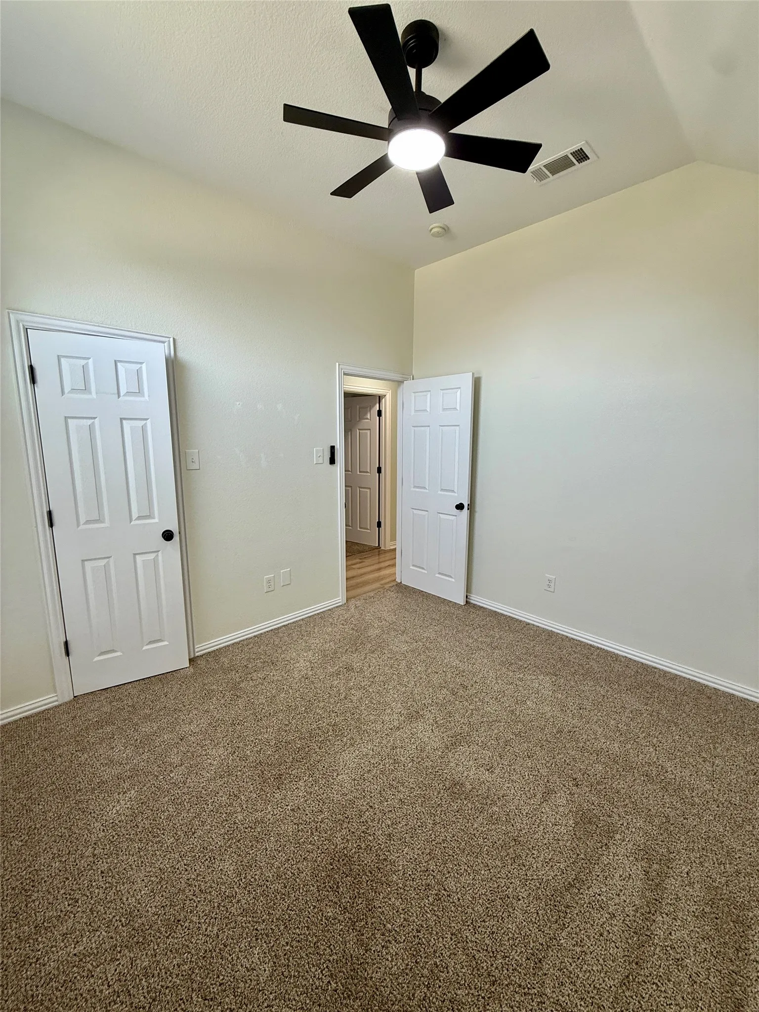 Spacious room featuring vaulted ceilings, a contemporary ceiling fan with integrated lighting, and plush carpeting