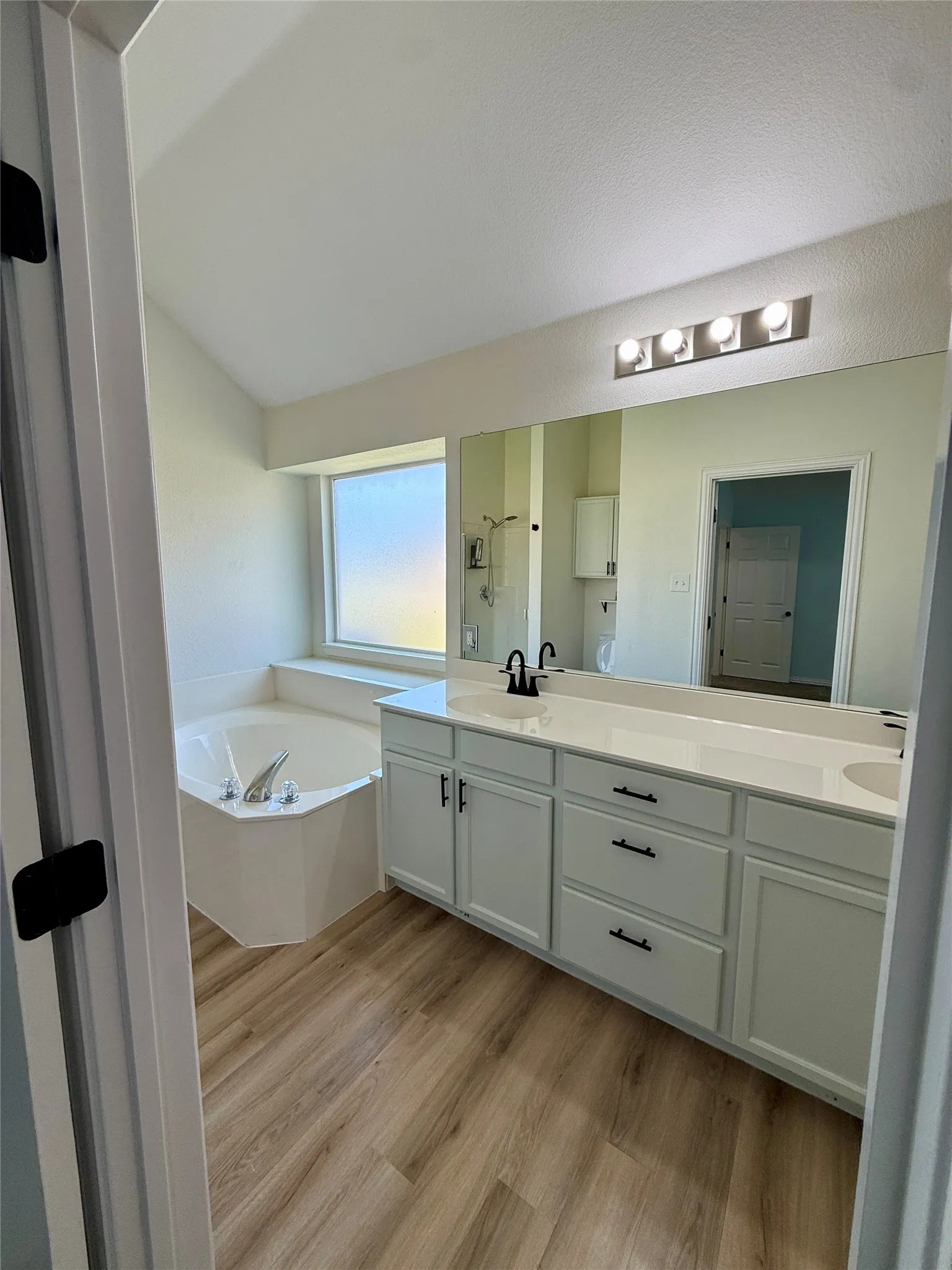 Bathroom featuring a corner soaking tub, dual vanity with white cabinetry, light countertops, and wood-finish flooring