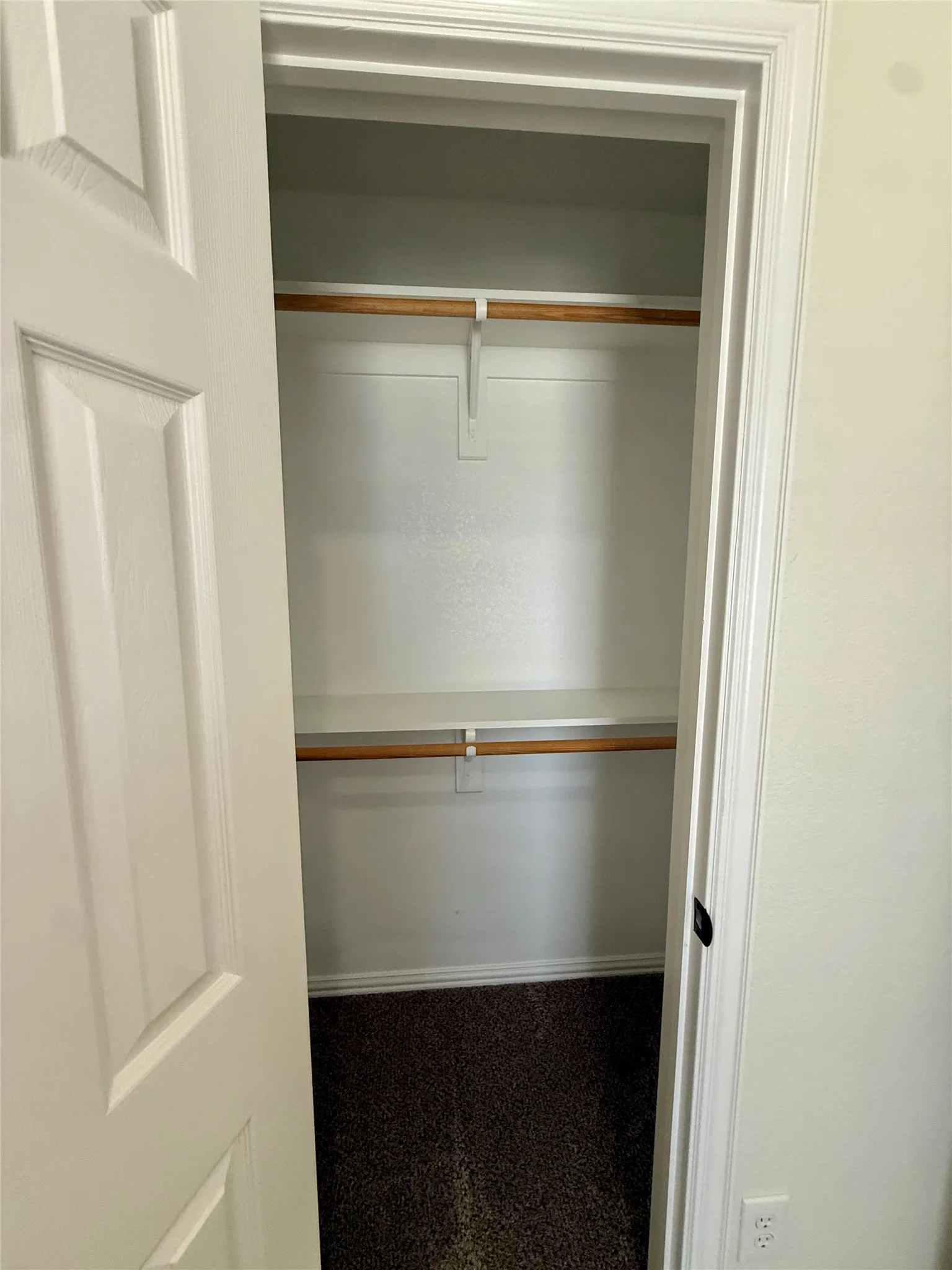 Recessed closet with white interior walls, featuring two wooden hanging rods and a white built-in shelf