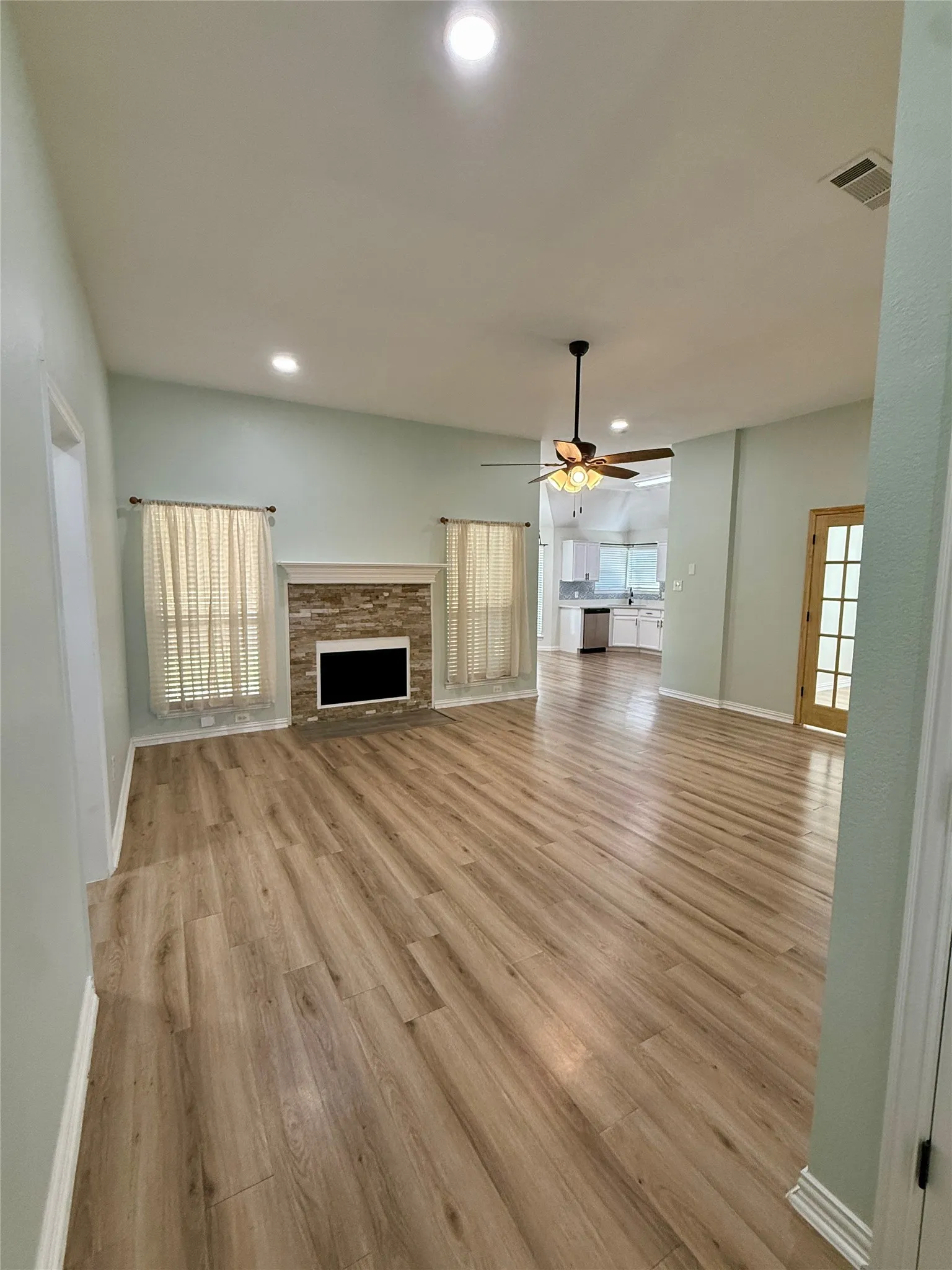 Spacious living area featuring wood-finish flooring, a stone-accented fireplace, vaulted ceiling with recessed lighting, and a ceiling fan