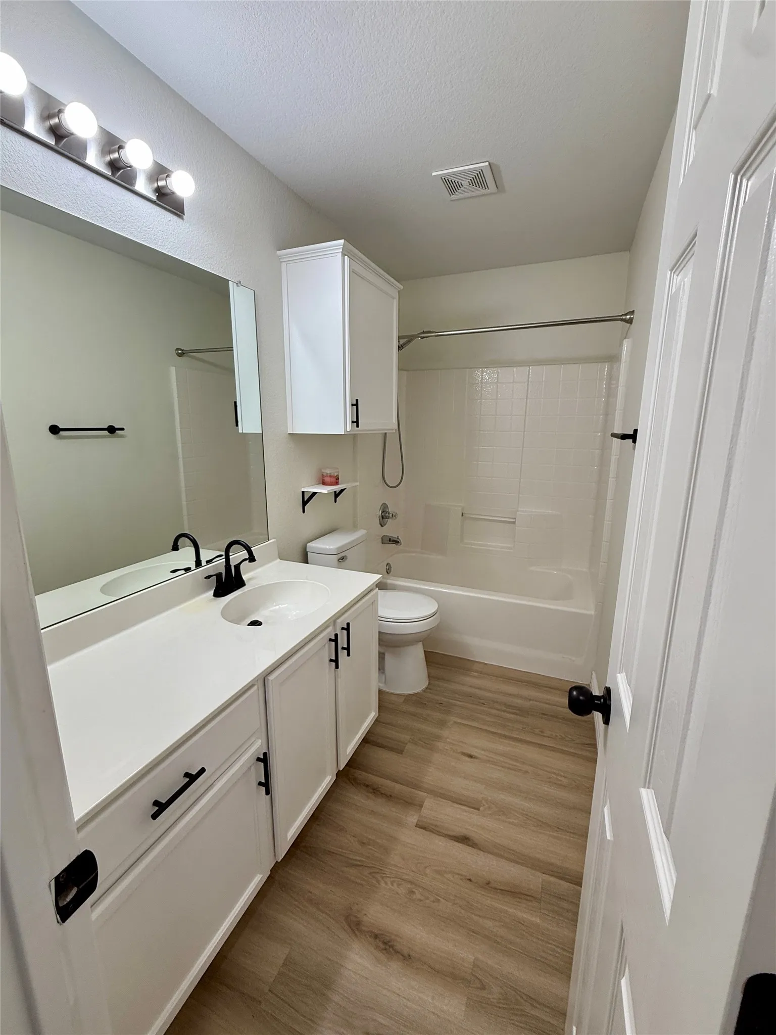 Bathroom featuring a white vanity with an integrated sink, black hardware, and a matching over-toilet cabinet