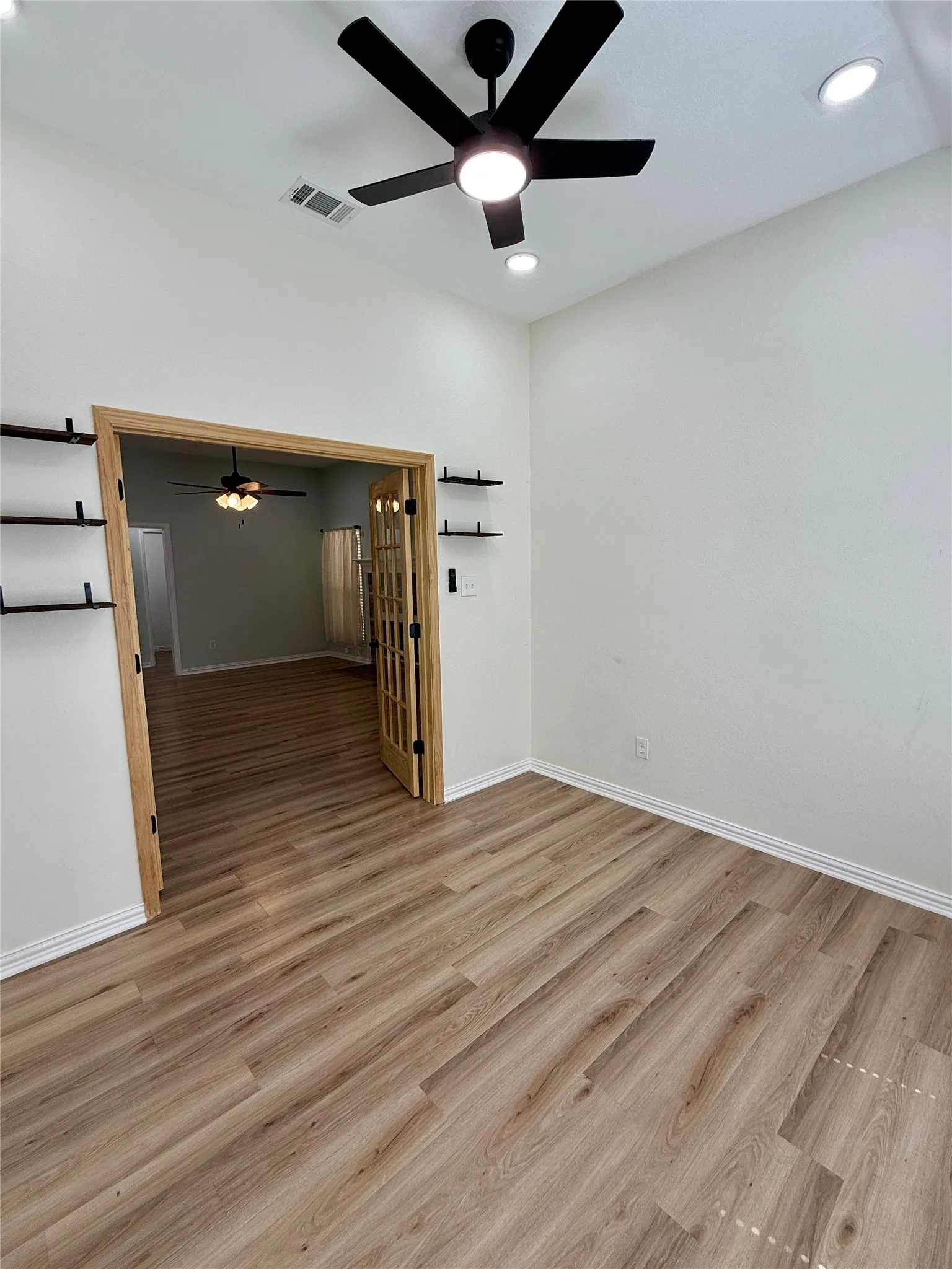 Bright room featuring wood-finish flooring, a modern black ceiling fan, recessed lighting, and built-in floating shelves