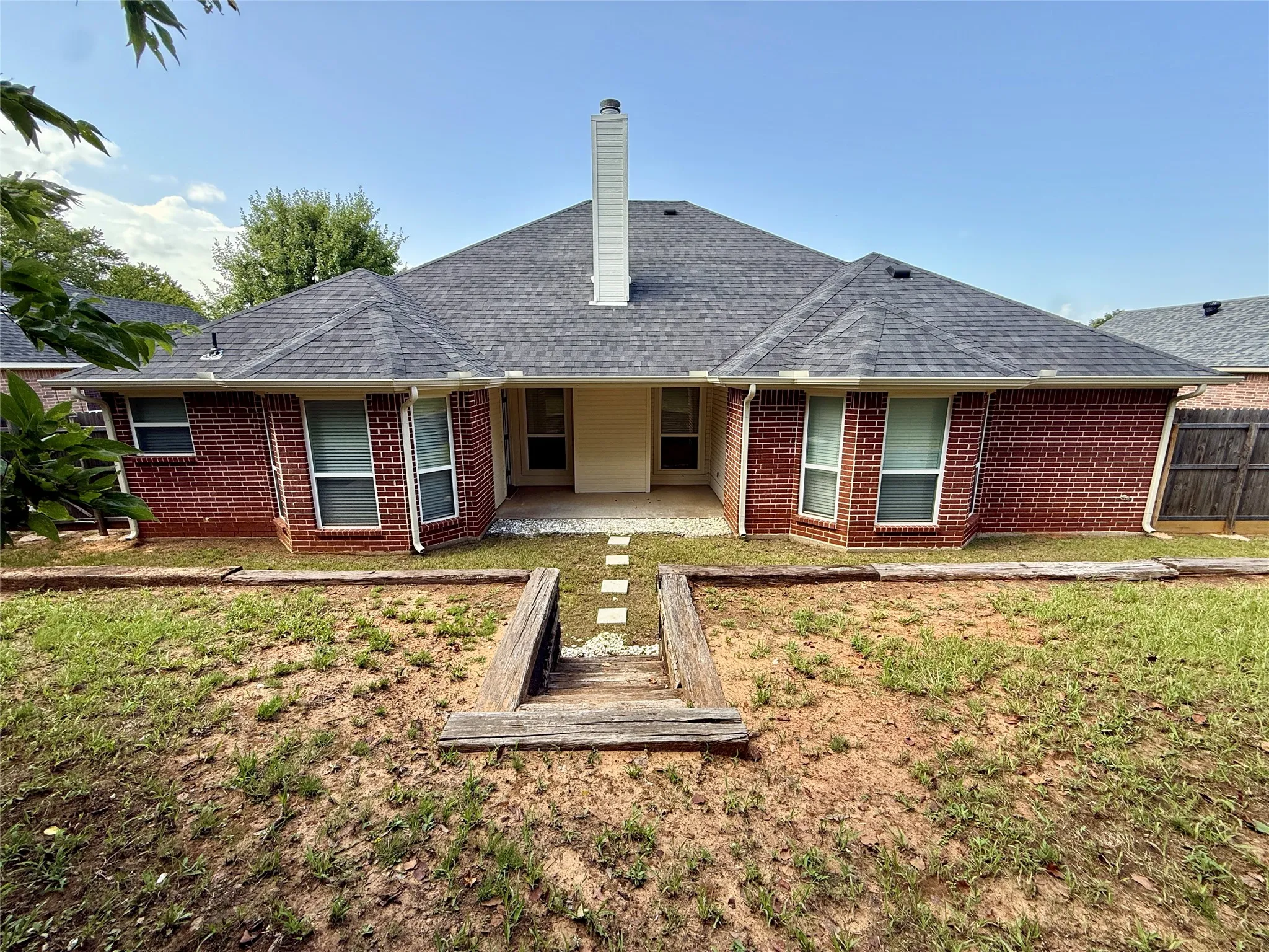 Brick exterior featuring a covered patio, dark shingle roof, and a central chimney