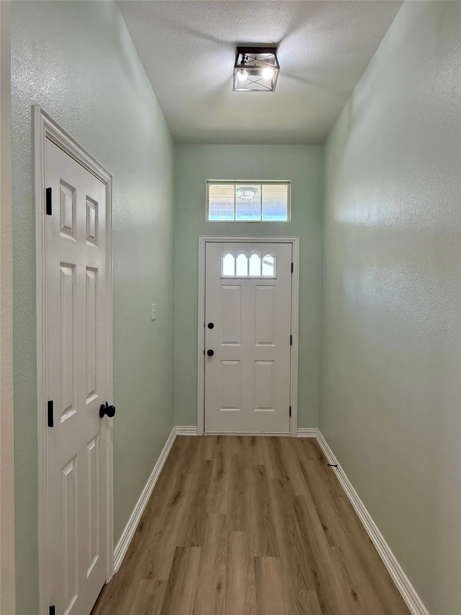 Entryway featuring light green walls, wood-finish flooring, and white baseboards