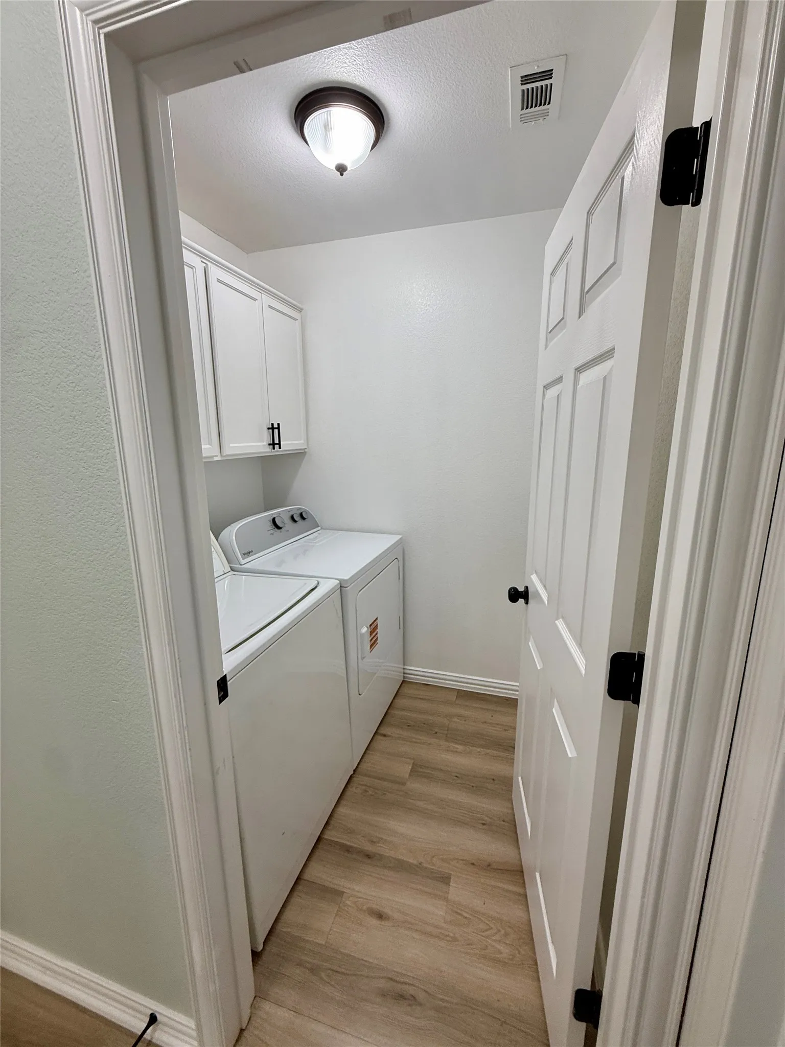 Dedicated laundry area featuring wood-finish flooring, white cabinetry with dark hardware, and a ceiling-mounted light fixture