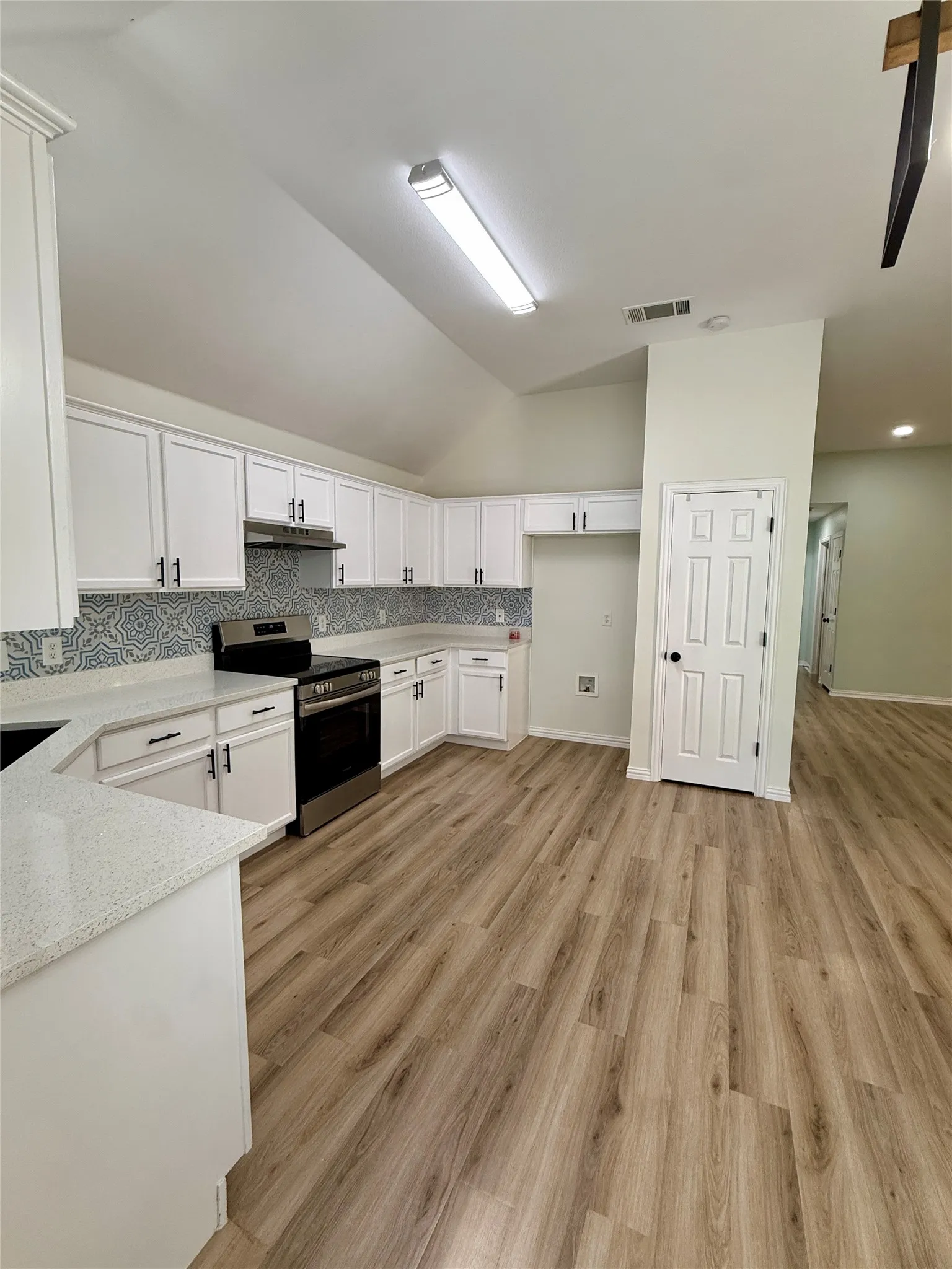 Modern kitchen featuring white cabinetry, light-toned countertops, a patterned tile backsplash, and wood-finish flooring