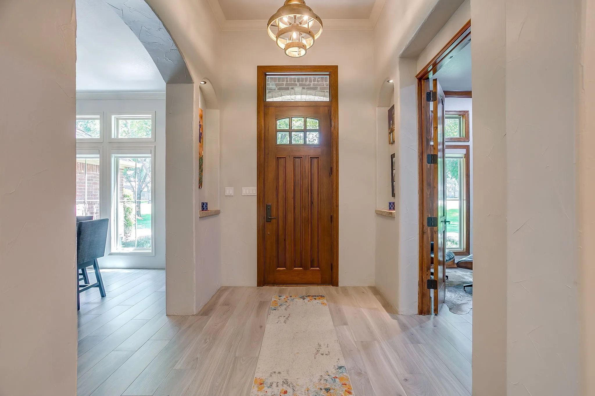 Foyer with decorative lighted niches, arched access to the formal dining, and decorative wood stain trim into the home office