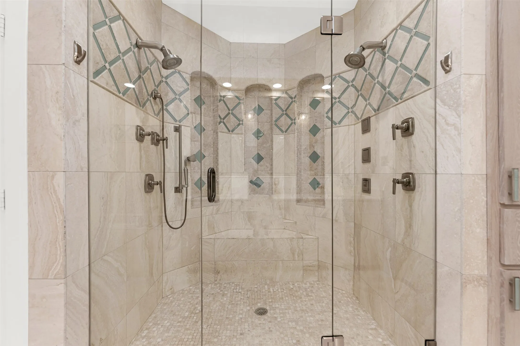 The glass-enclosed shower boasts dual heads, a built-in bench, and delicate mosaic-tiled niches. Indulge in a hot, steam-filled rinse that feels like a personal resort experience after a busy day.