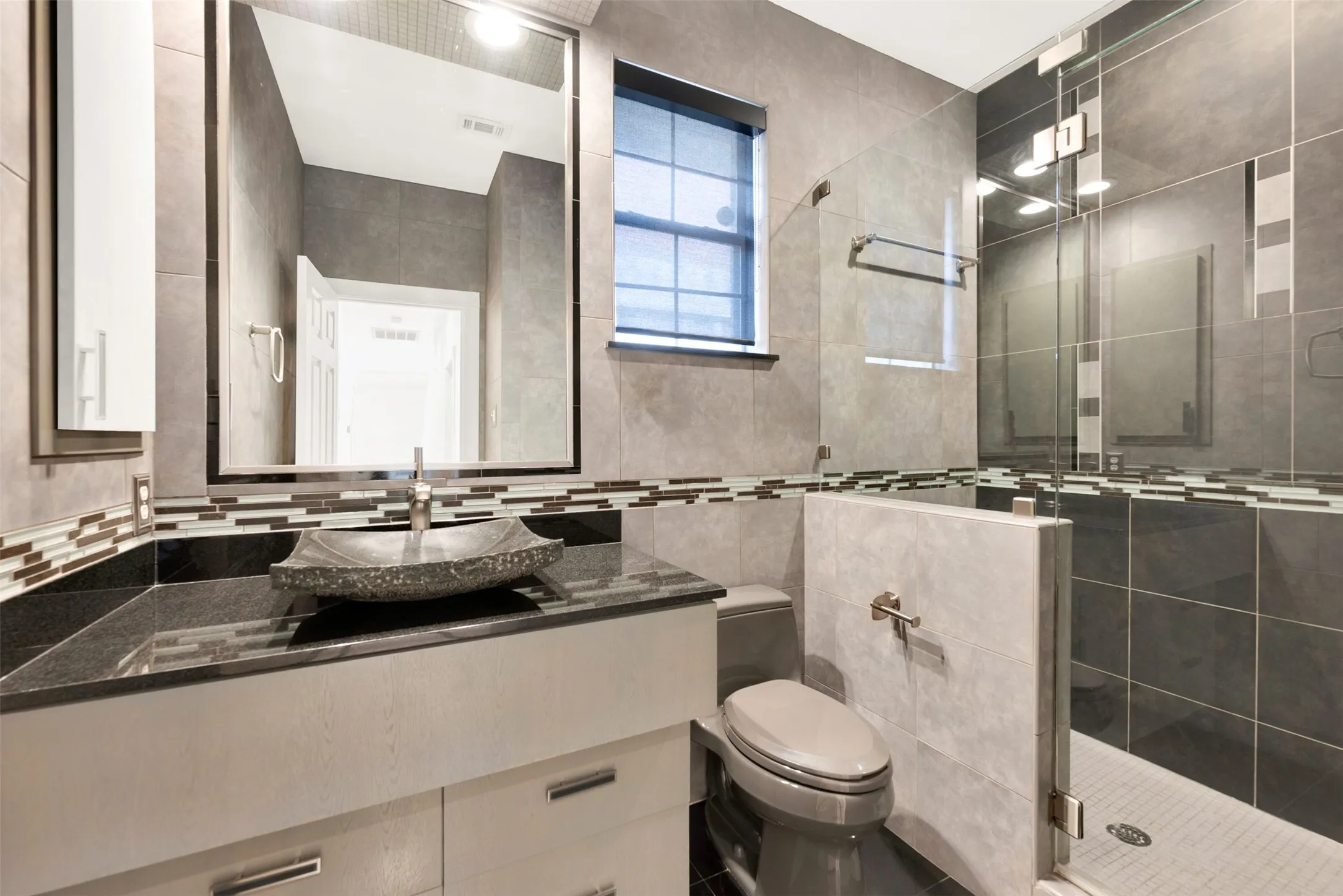 Sleek, slate-gray tiling wraps this space in a contemporary embrace, anchored by a striking textured stone vessel sink. Pamper your weekend visitors with a sophisticated, private retreat that feels just like a boutique design hotel
