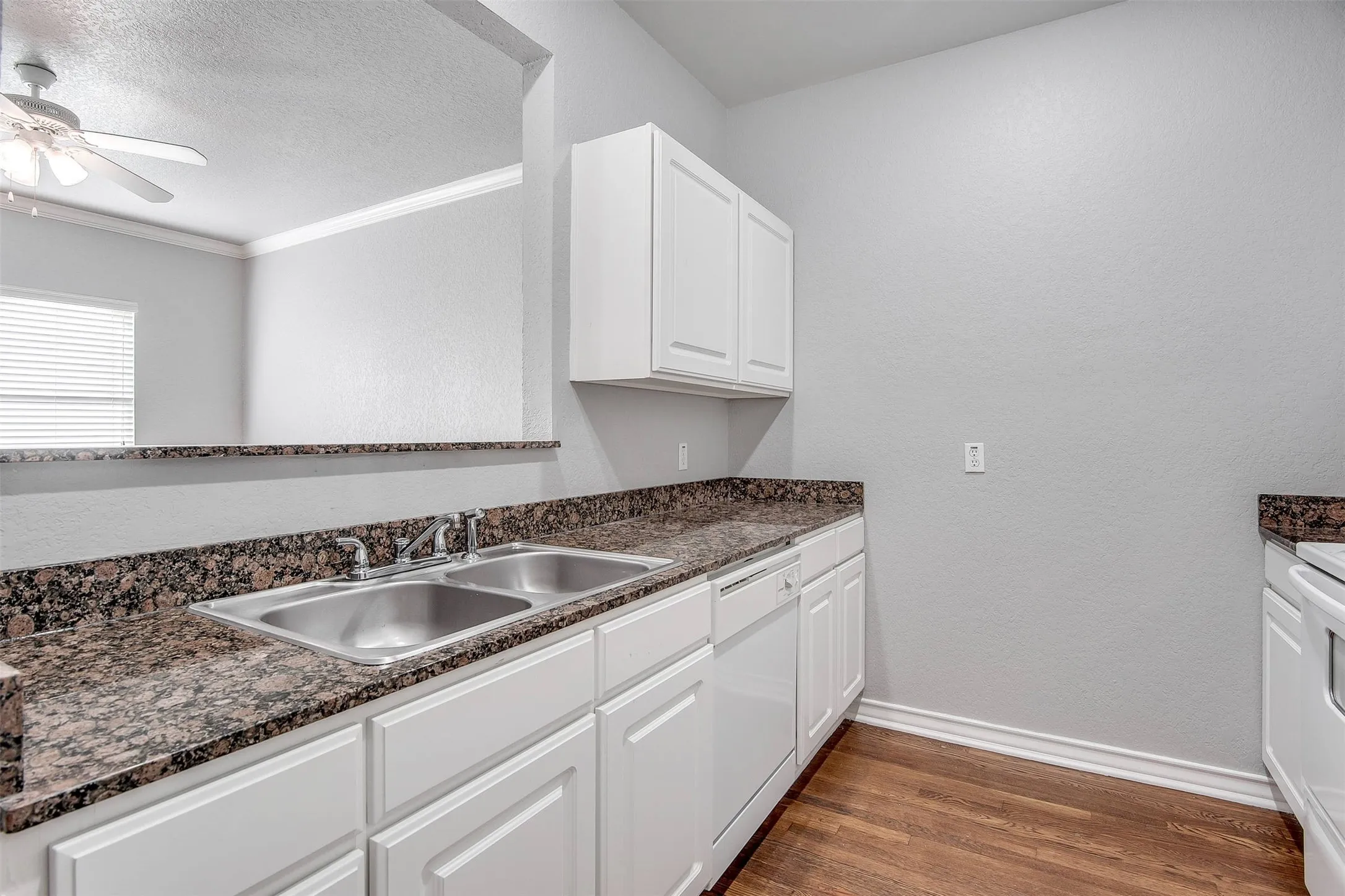 Kitchen featuring white cabinetry, a double basin stainless steel sink, dark granite-finish countertops, white appliances, and wood-finish flooring