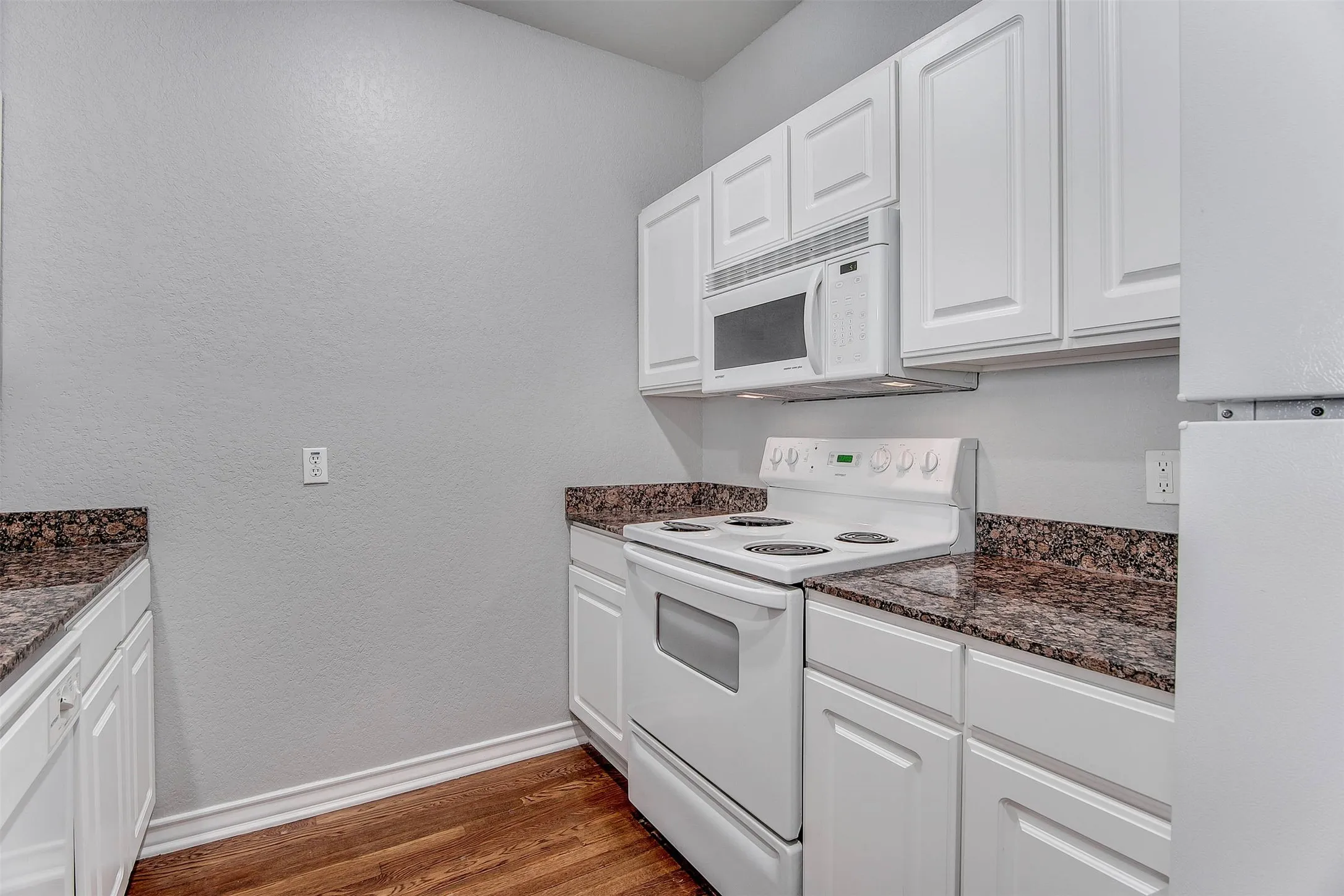 Kitchen featuring white cabinetry, dark speckled countertops, white electric range, and an over-the-range microwave