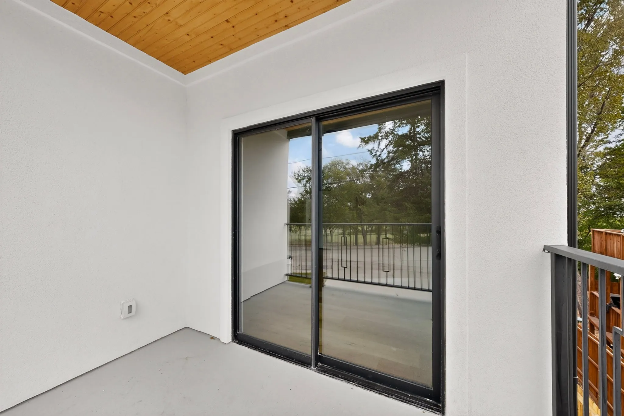 Private balcony featuring a wood plank ceiling, sliding glass door with black trim, and metal railings