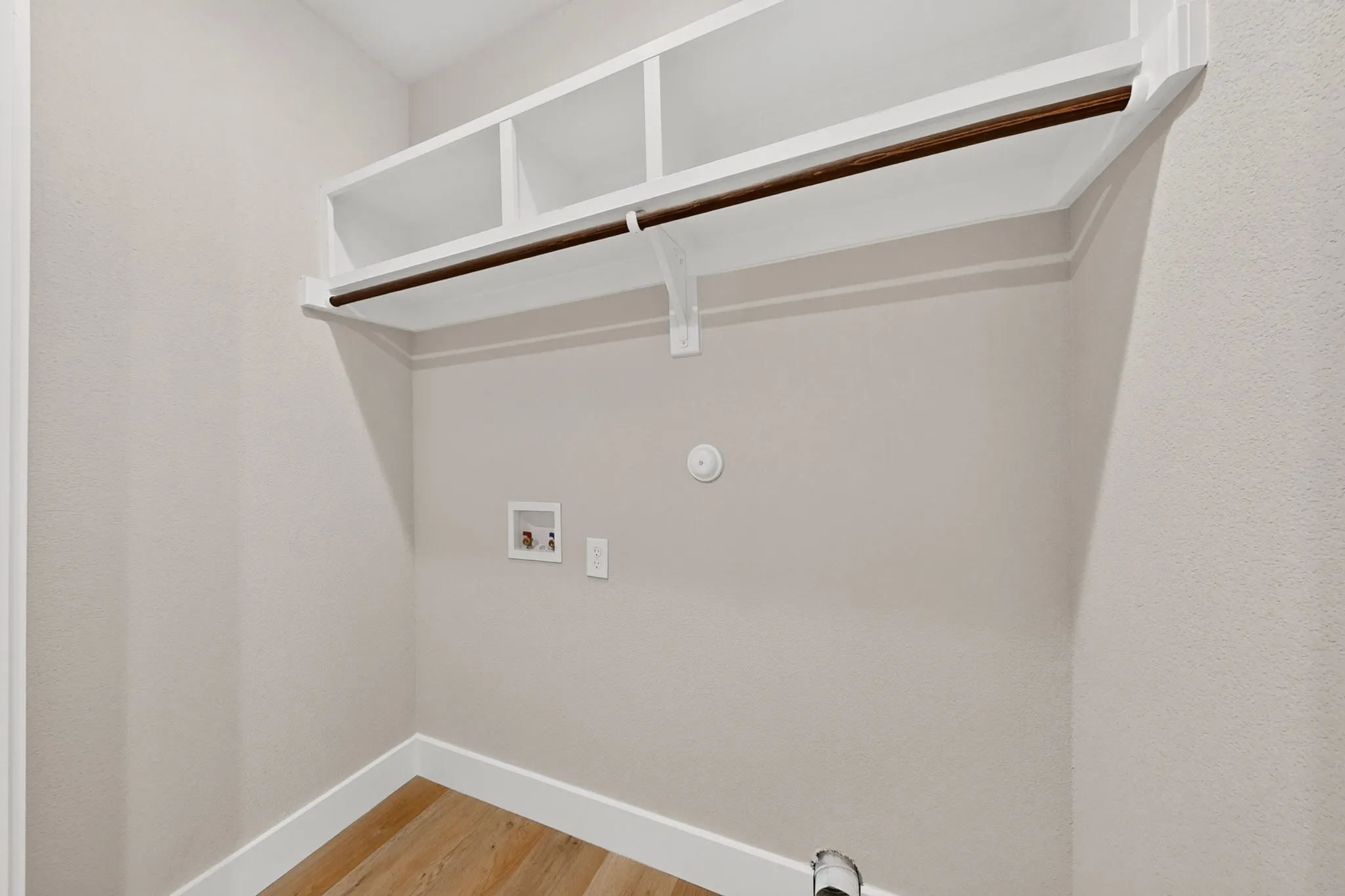 Laundry area featuring integrated shelving, a clothes rod, and wood-finish flooring