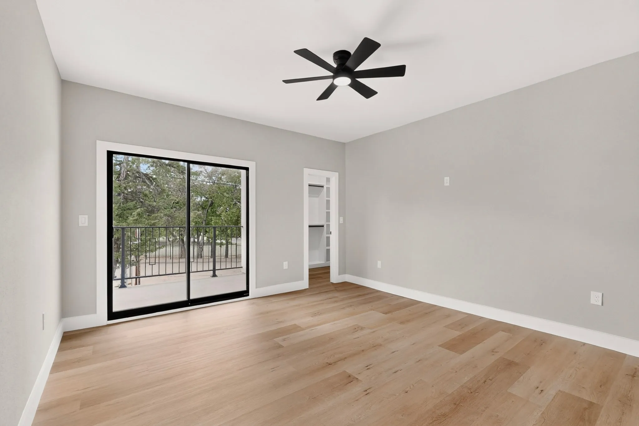 Light wood-finish flooring, sliding glass doors, white trim, and a black ceiling fan